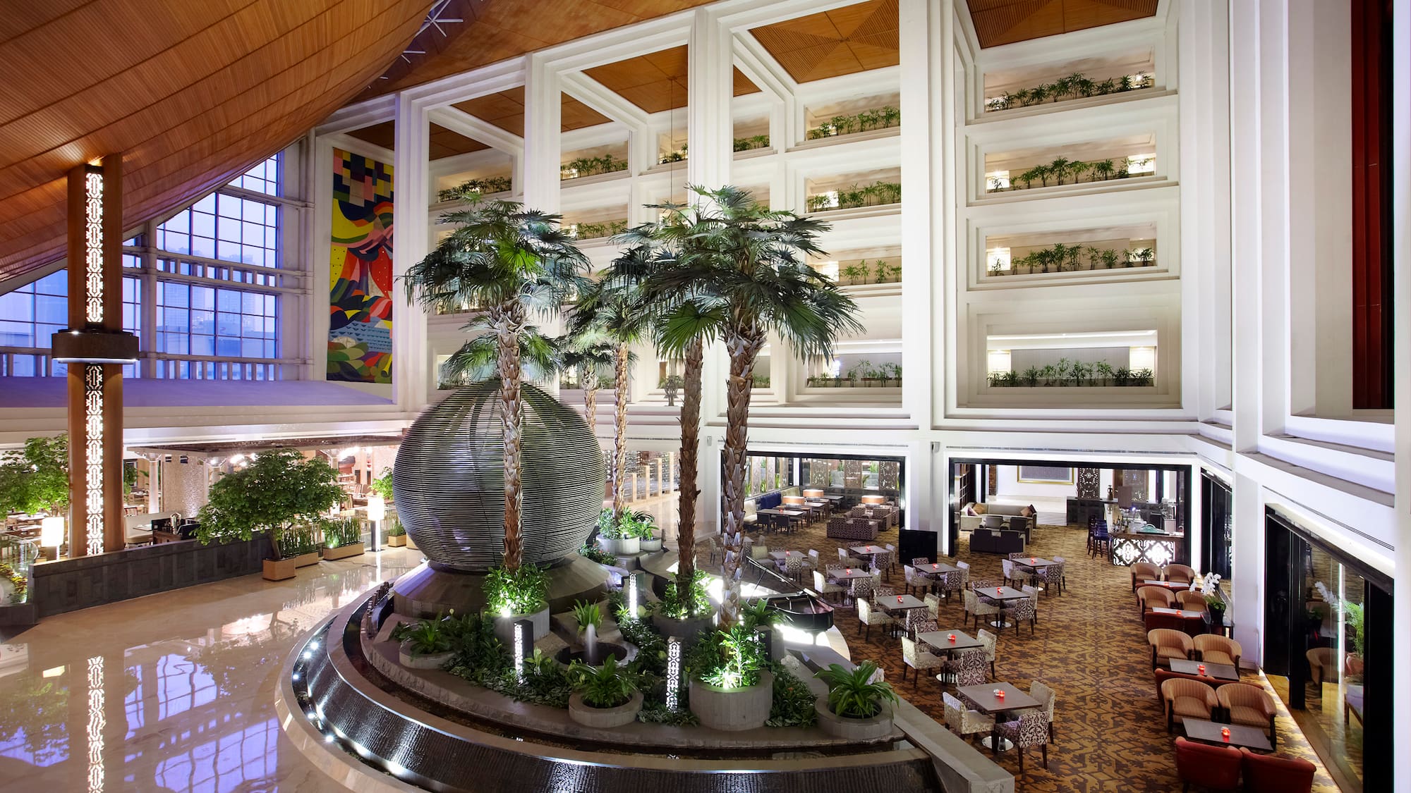 Spacious hotel lobby with palm trees, decorative fountain, and lounge seating.