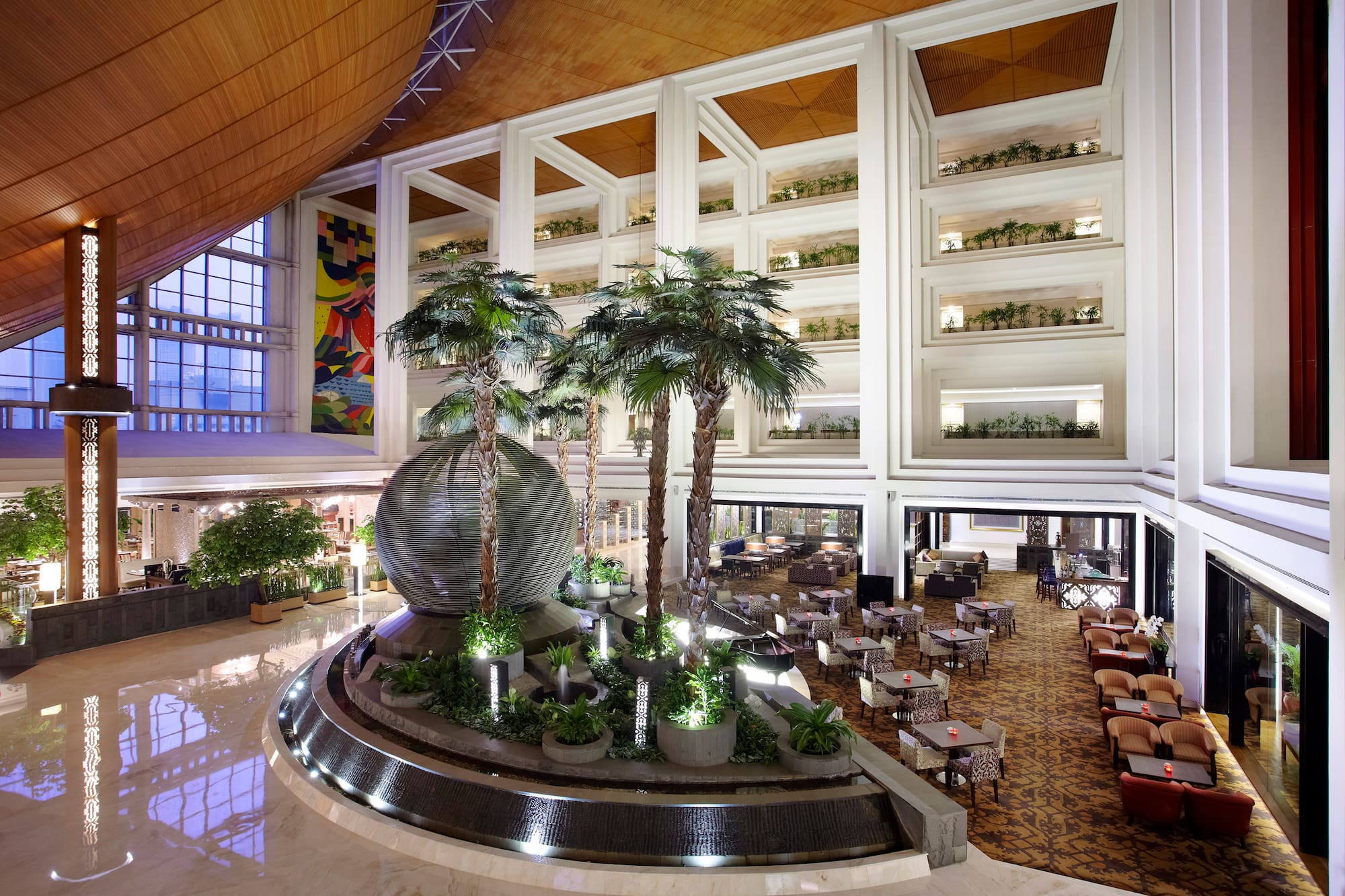 Spacious hotel lobby with palm trees, decorative fountain, and lounge seating.