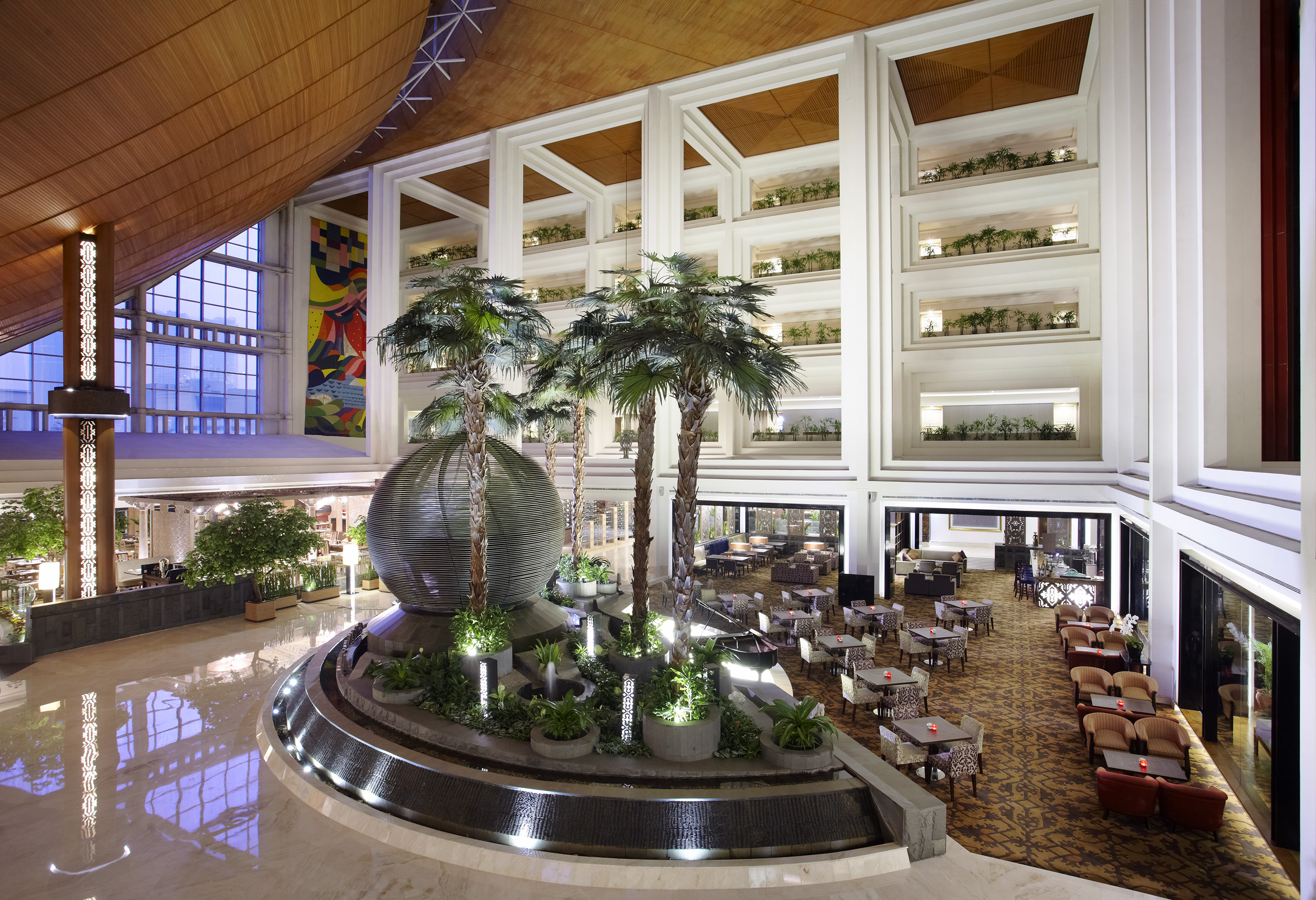 Spacious hotel lobby with palm trees, decorative fountain, and lounge seating.