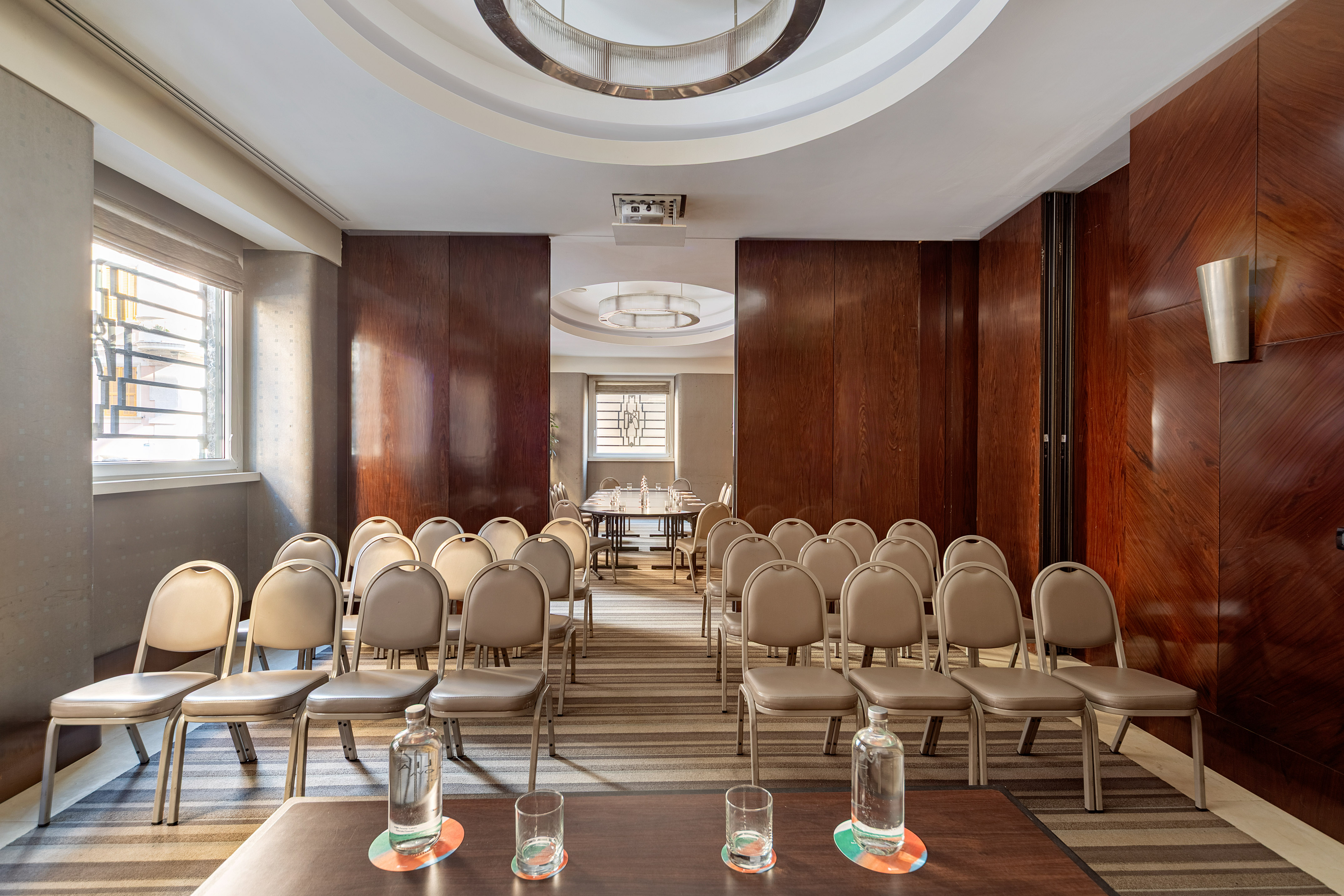 Theater-style conference room with beige chairs, wood paneling, and projector. - Madreperla - Meliá Genova, Genua