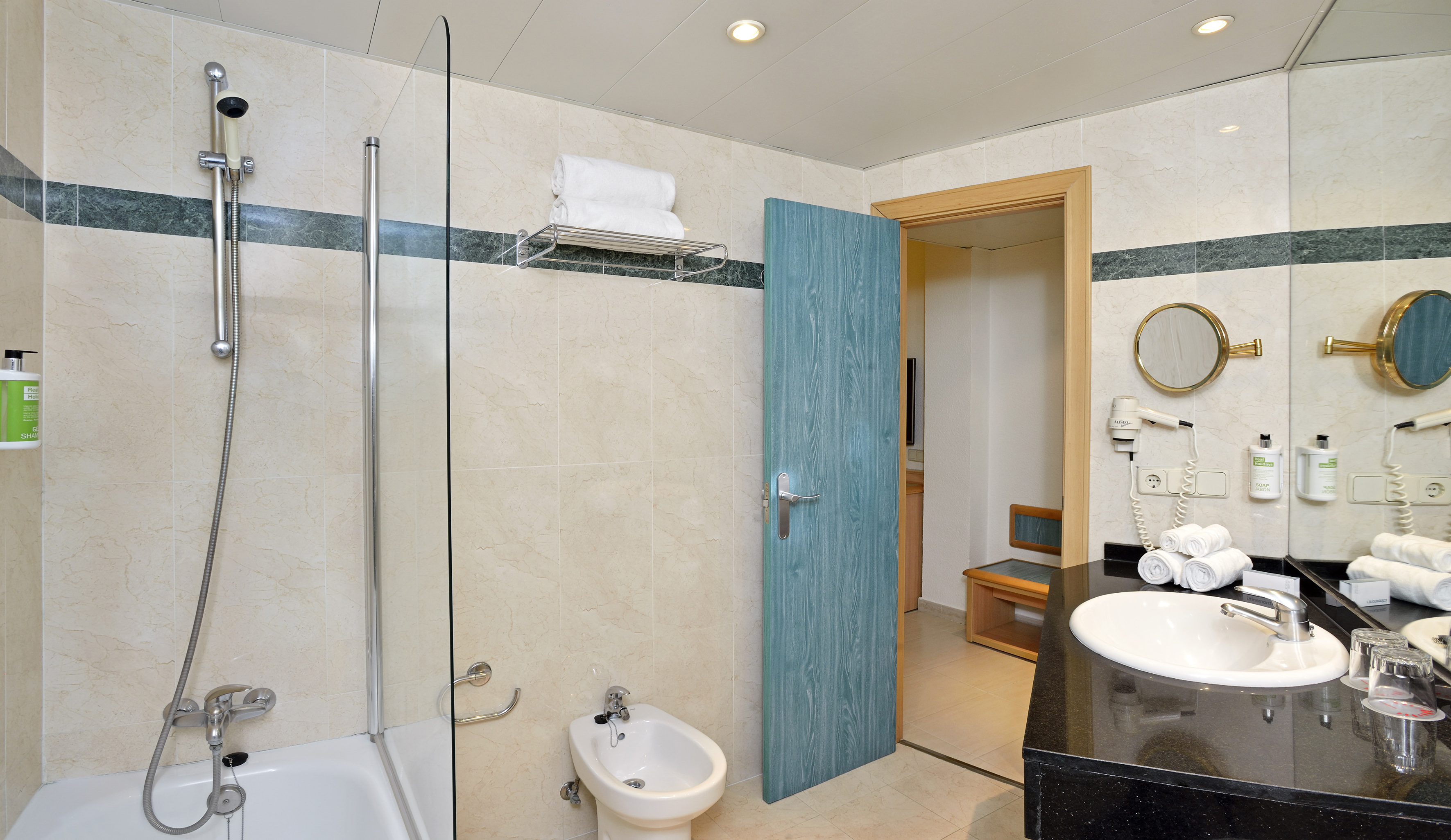 Hotel bathroom with tiled walls, bathtub, bidet, vanity sink, and blue door.