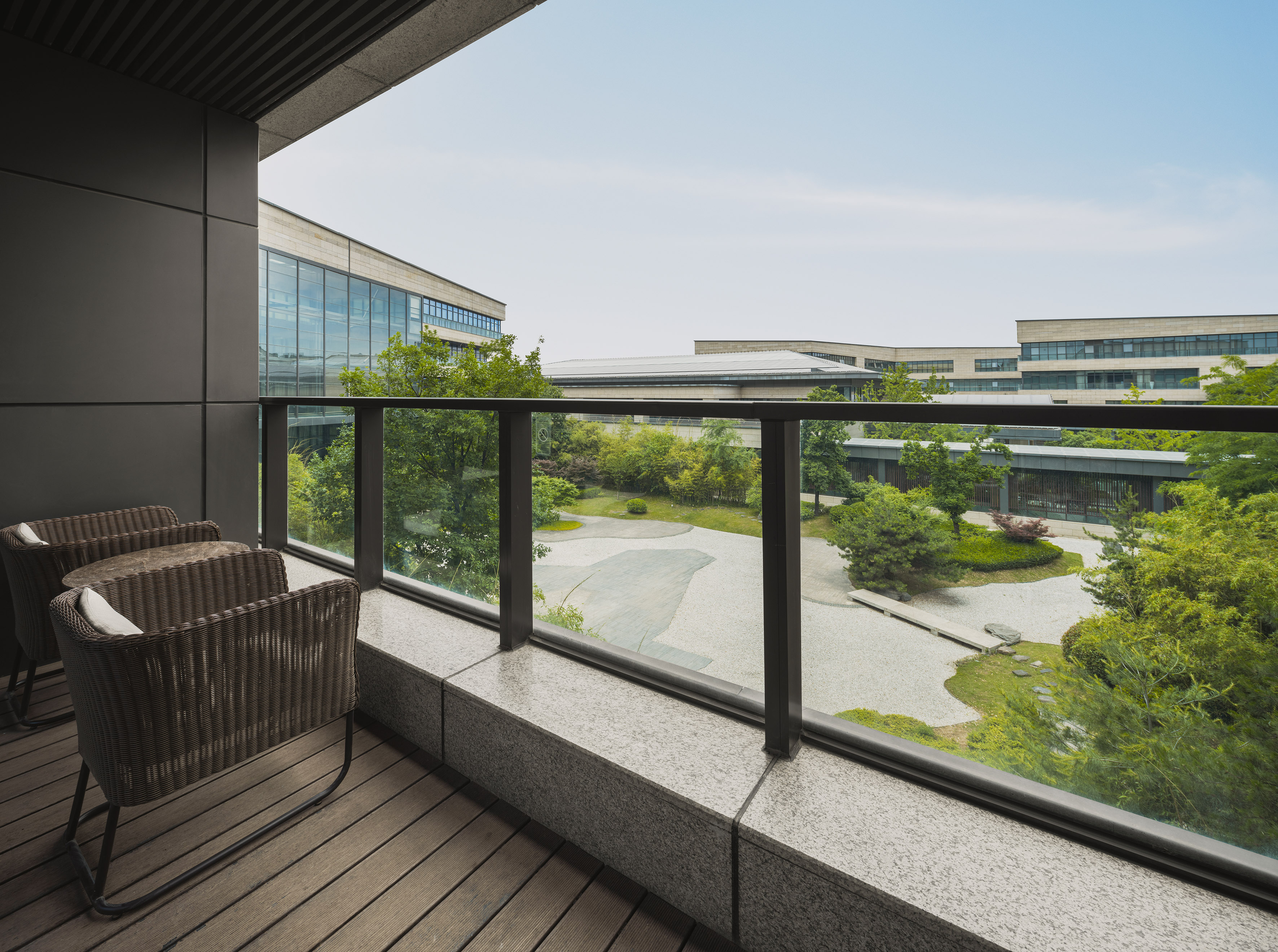 Modern hotel balcony with wicker chairs, garden view, and corporate buildings.