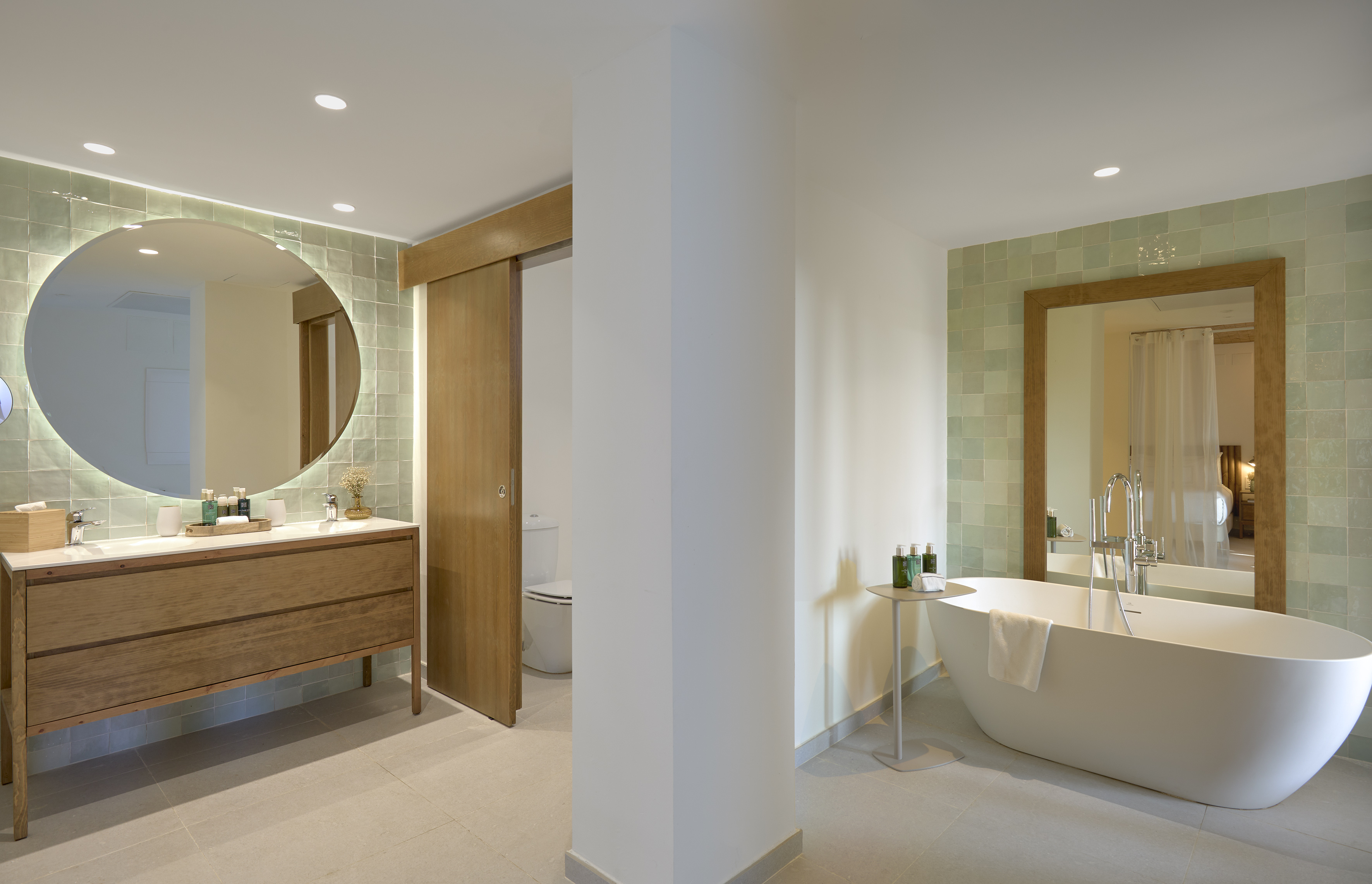 Modern bathroom with round backlit mirror, wood vanity, and freestanding bathtub.