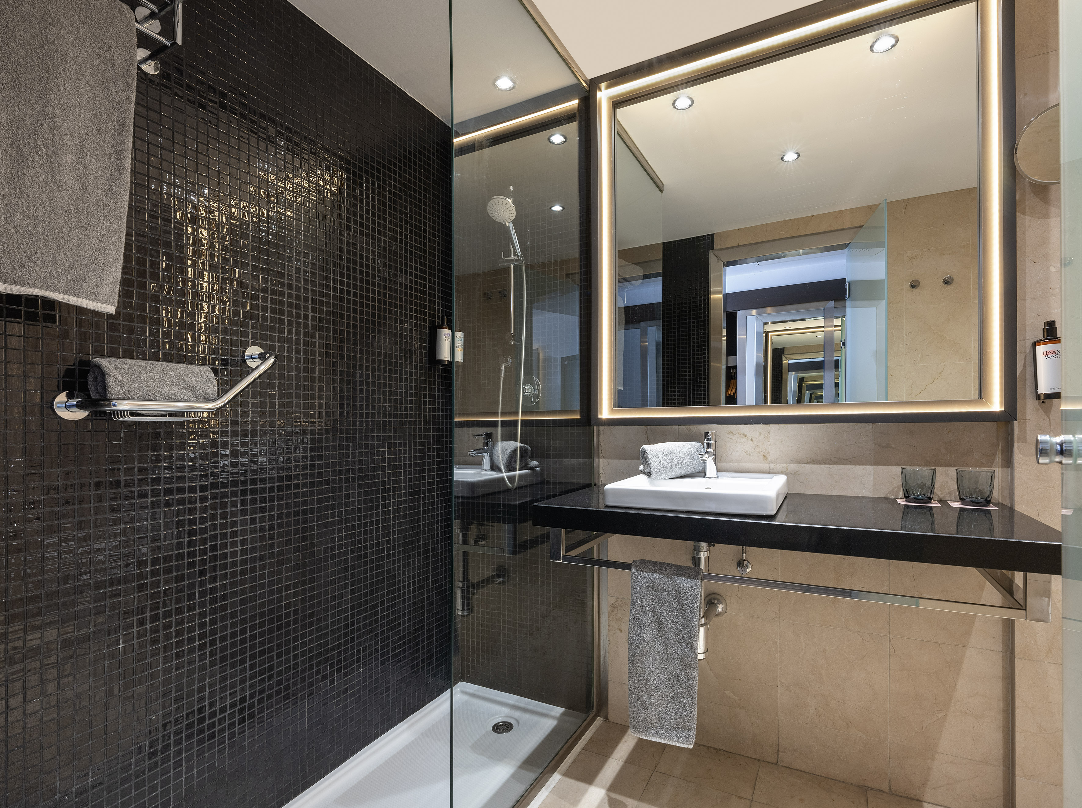 Sleek bathroom with black mosaic shower, illuminated mirror, and modern vanity.