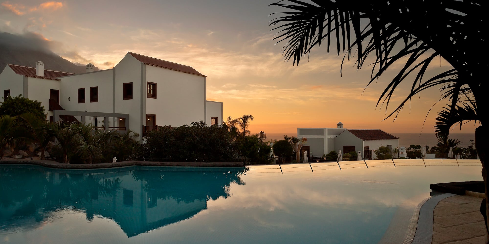 Tropical resort with infinity pool at sunset, white buildings, and ocean view.