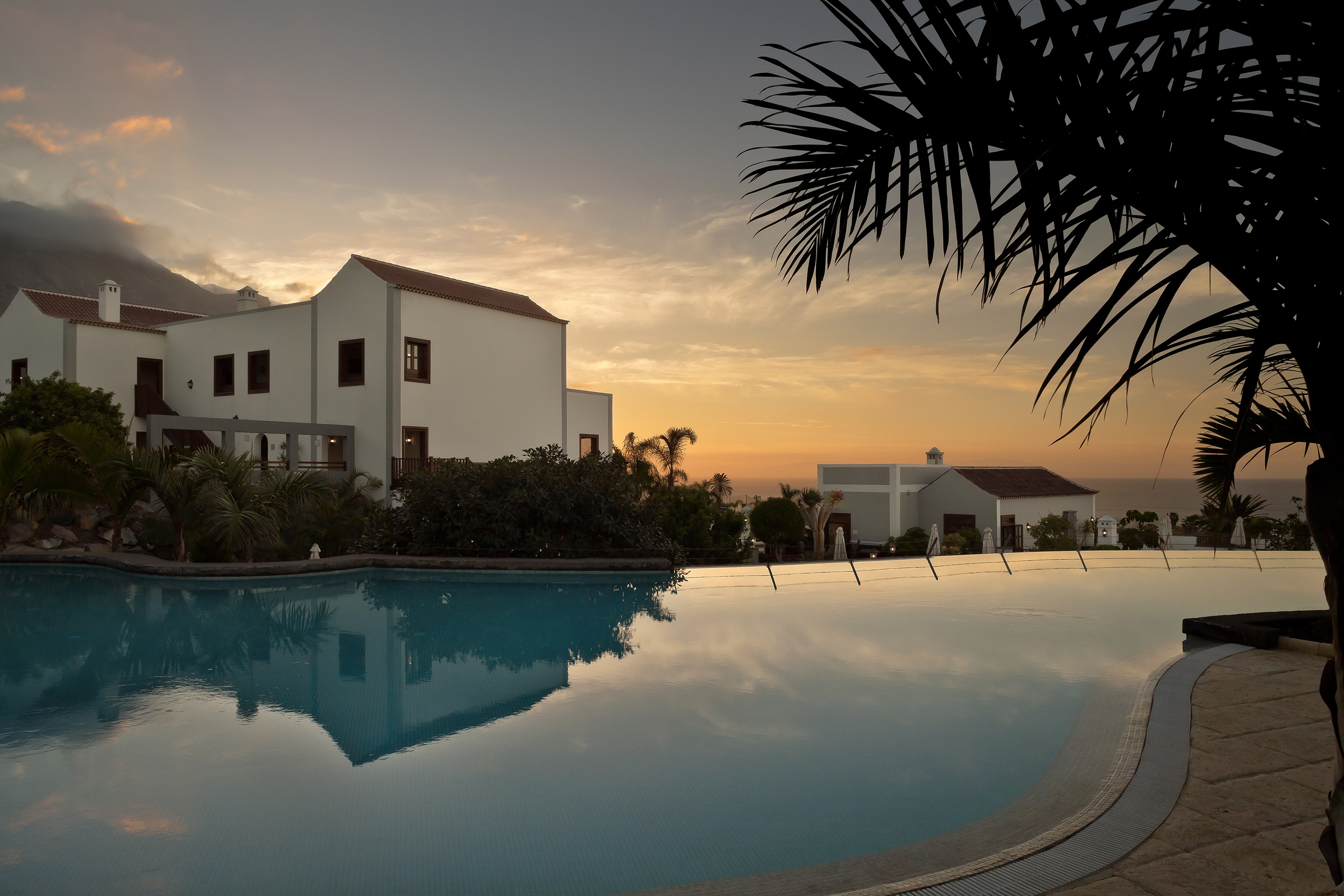 Tropical resort with infinity pool at sunset, white buildings, and ocean view.