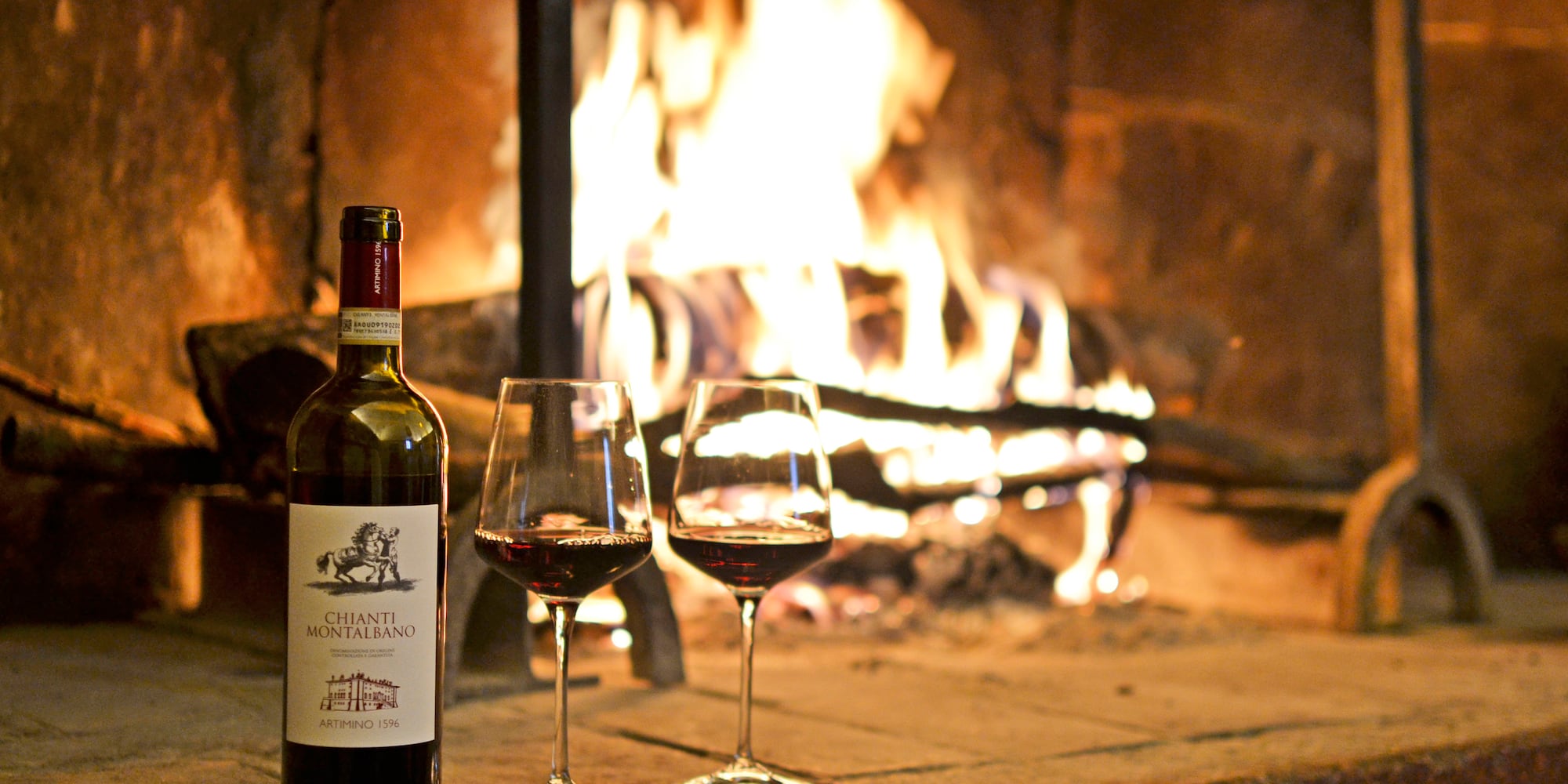 a bottle of wine and two glasses of wine in front of a fireplace