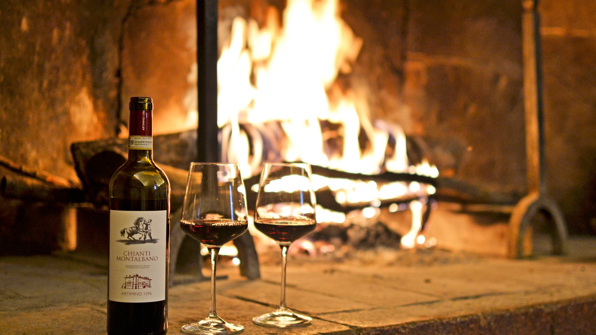 a bottle of wine and two glasses of wine in front of a fireplace