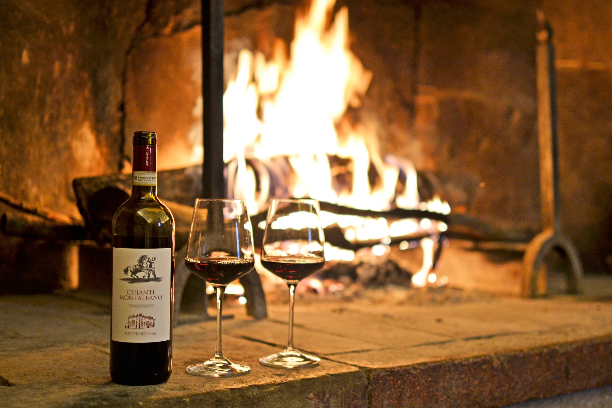 a bottle of wine and two glasses of wine in front of a fireplace