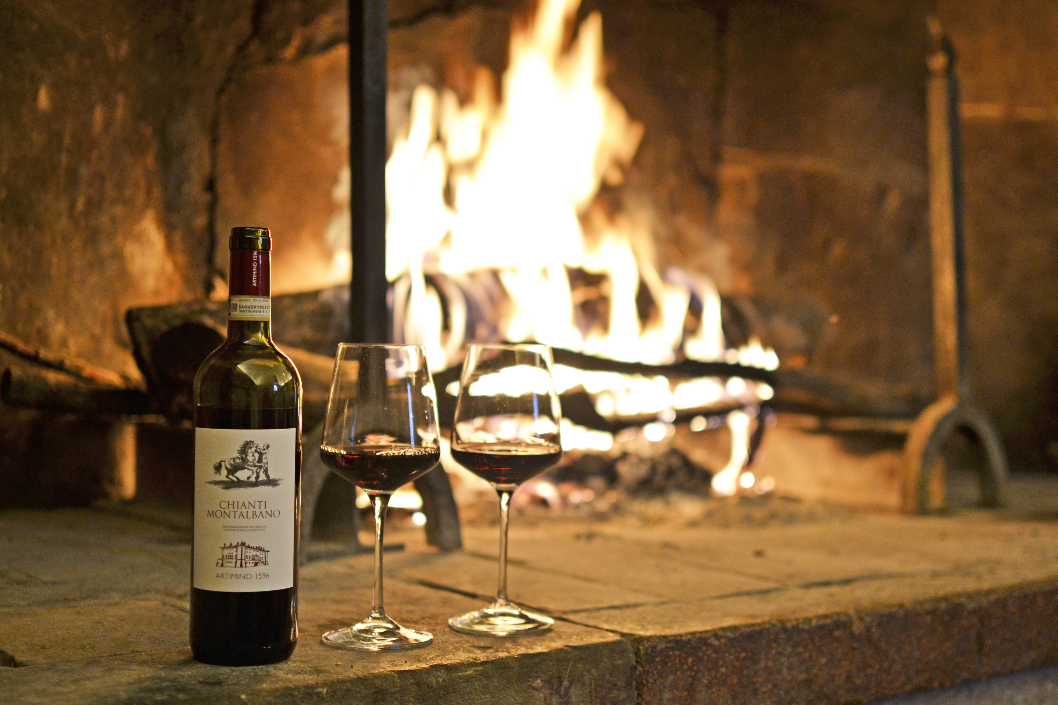 Chianti Montalbano red wine bottle, two glasses, roaring fireplace.