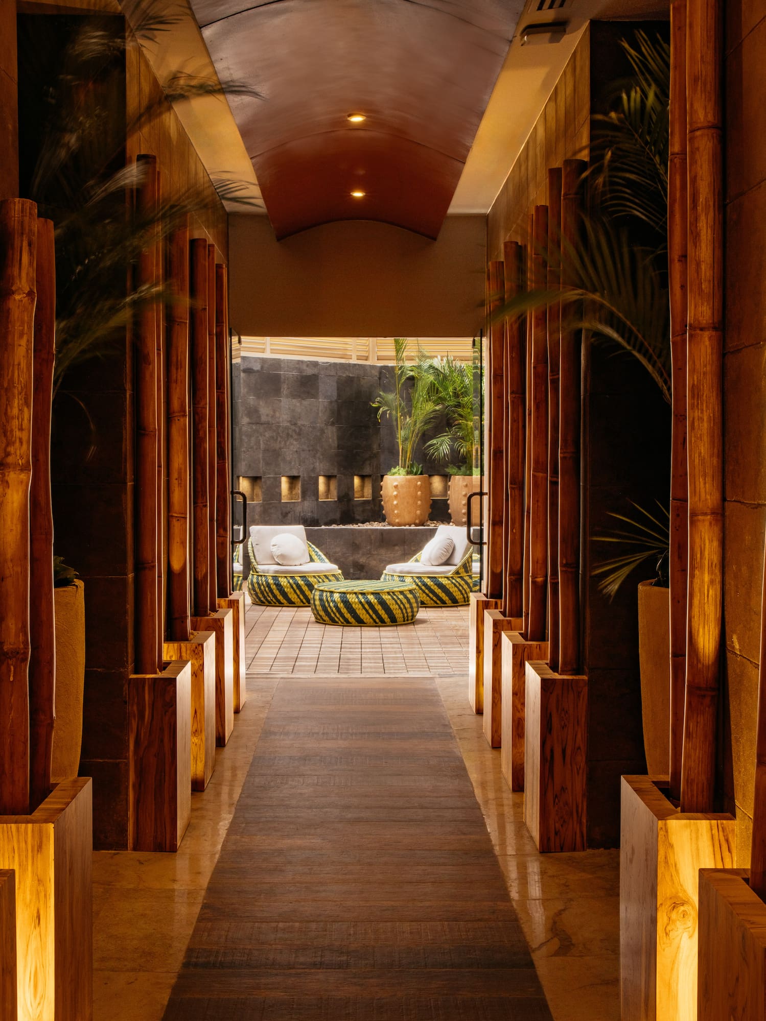 Warmly lit bamboo hallway leading to a tropical resort lounge area.