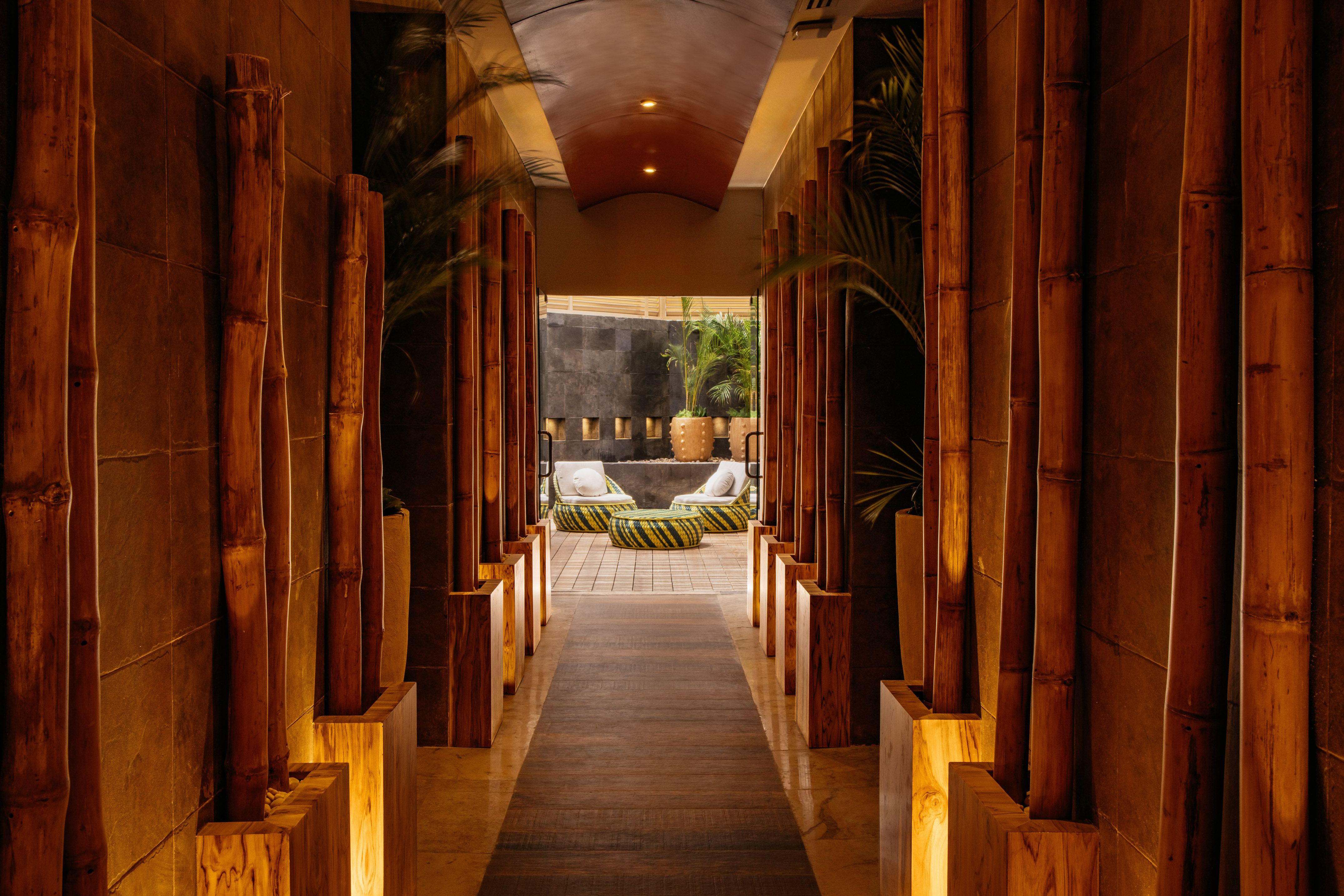 Warmly lit bamboo hallway leading to a tropical resort lounge area.