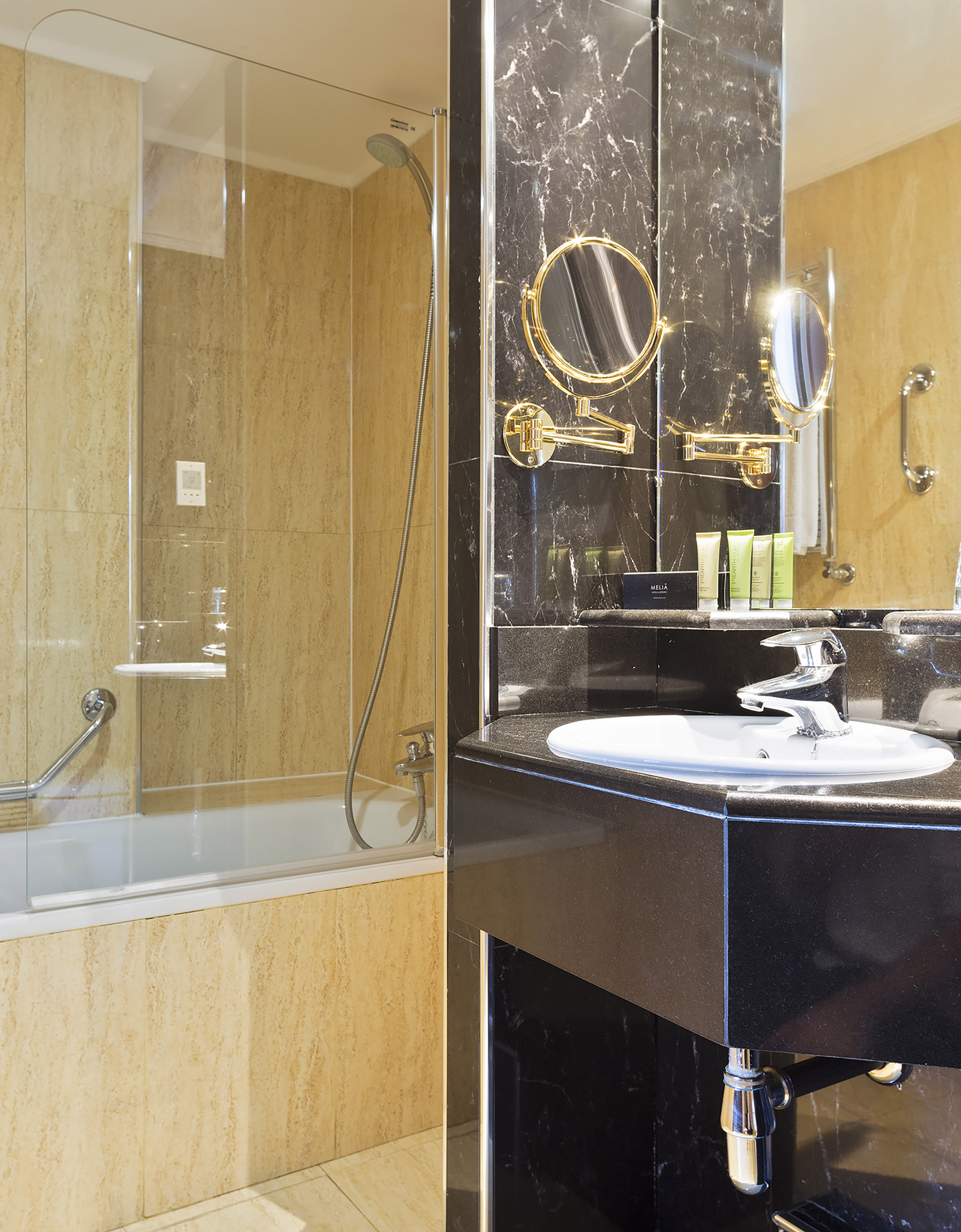 Modern hotel bathroom with black marble vanity, white sink, and beige shower-bathtub.