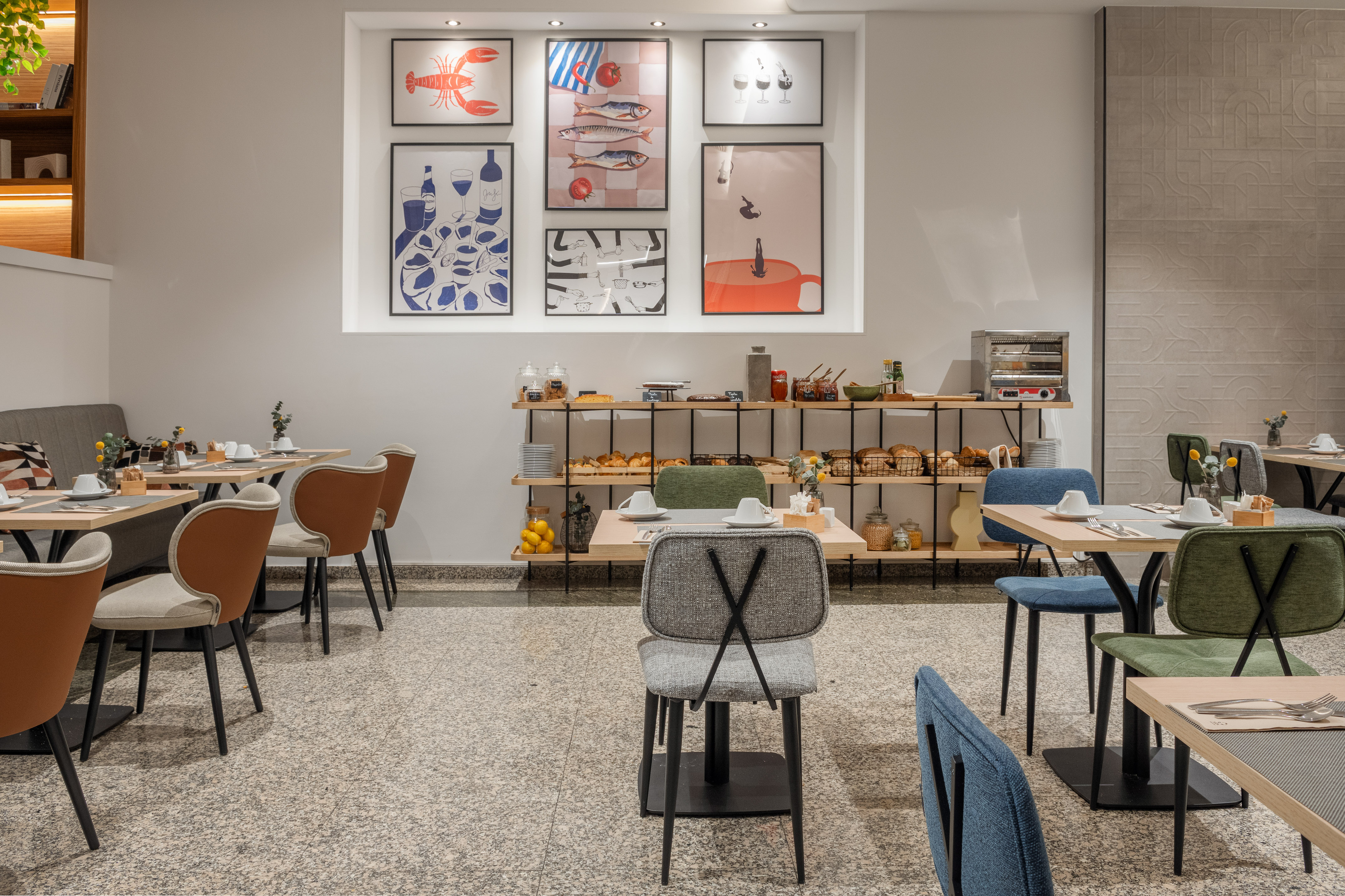 Hotel restaurant breakfast buffet with modern dining tables and wall art.