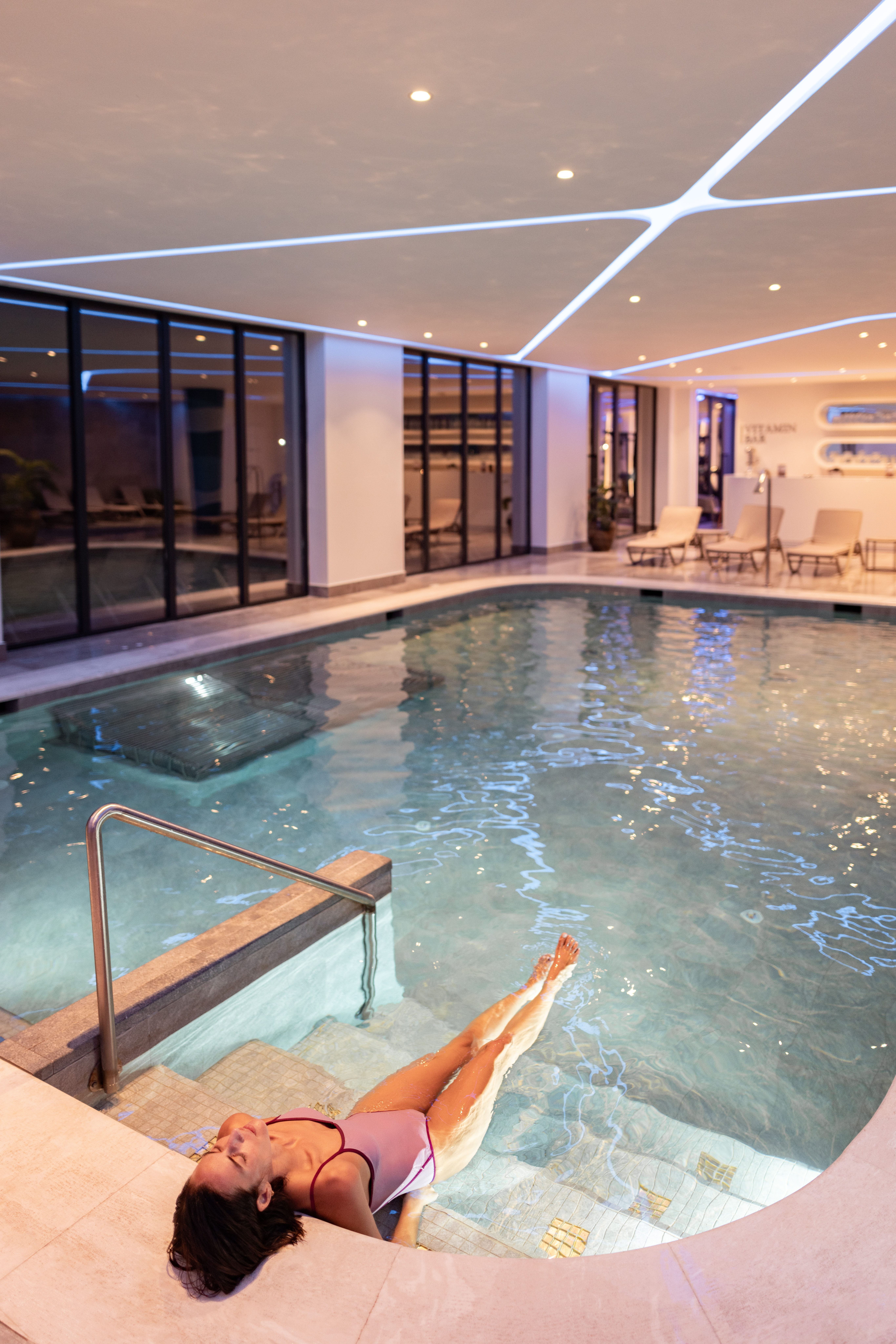 Relaxing woman in a pink swimsuit in a luxurious indoor spa pool.