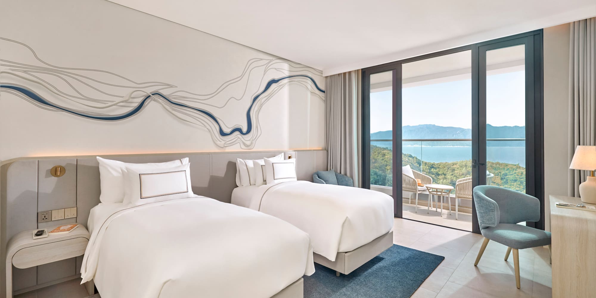 Modern hotel room with twin beds, balcony, and ocean mountain views.