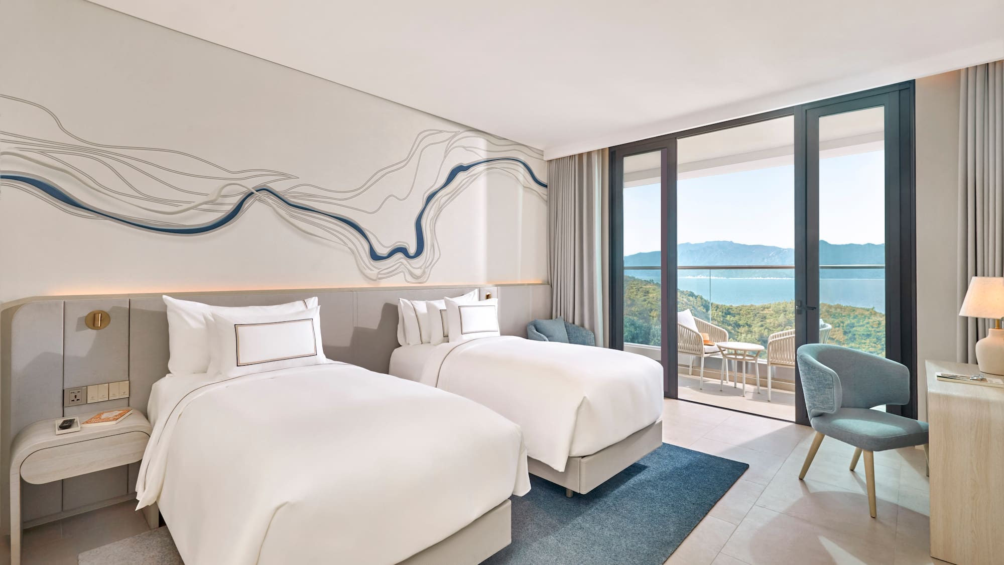 Modern hotel room with twin beds, balcony, and ocean mountain views.