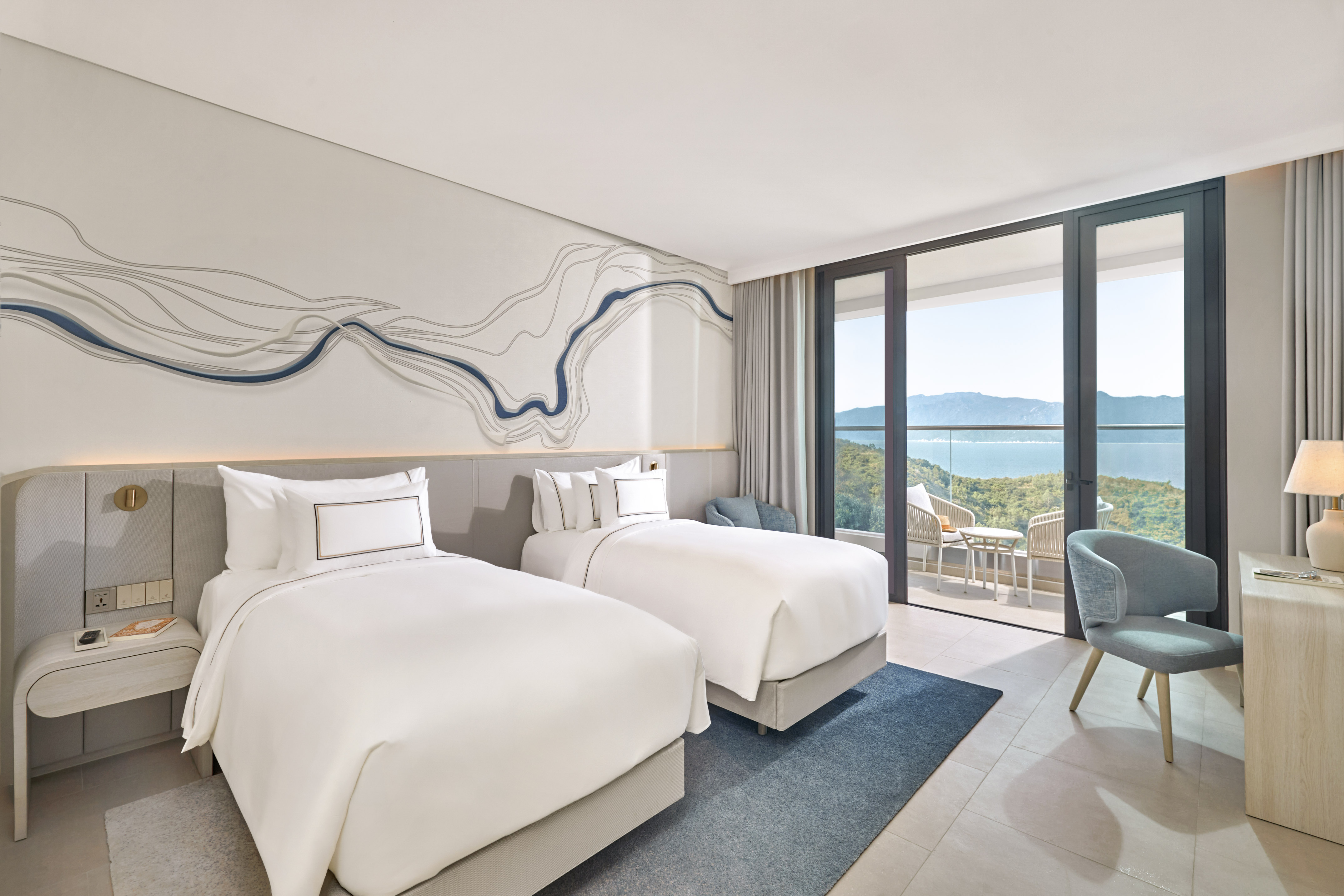 Modern hotel room with twin beds, balcony, and ocean mountain views.