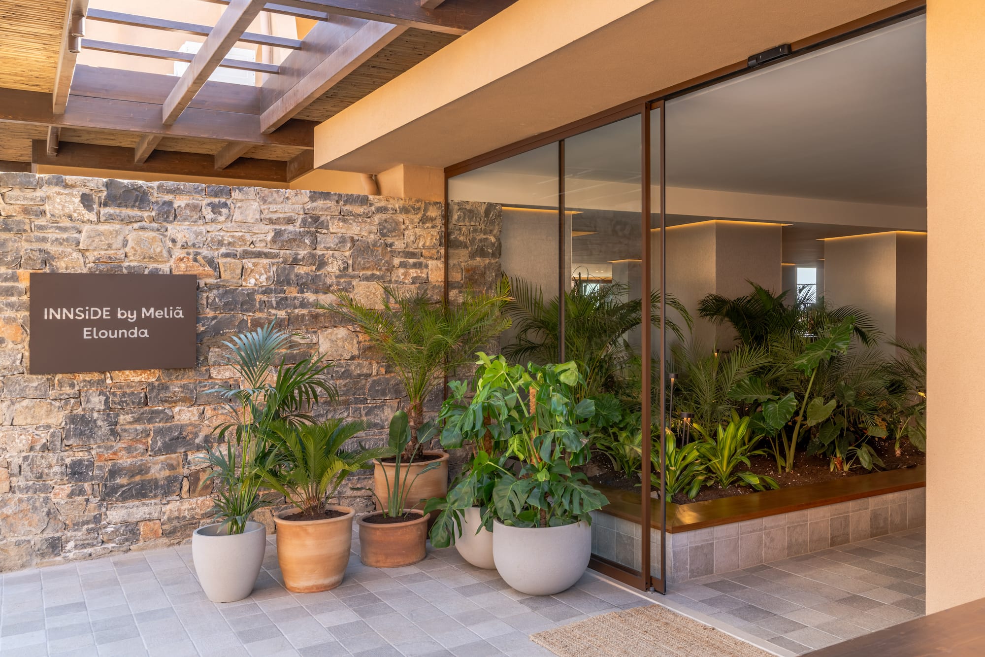 INNSiDE by Meliã Elounda entrance with stone wall and tropical plants.