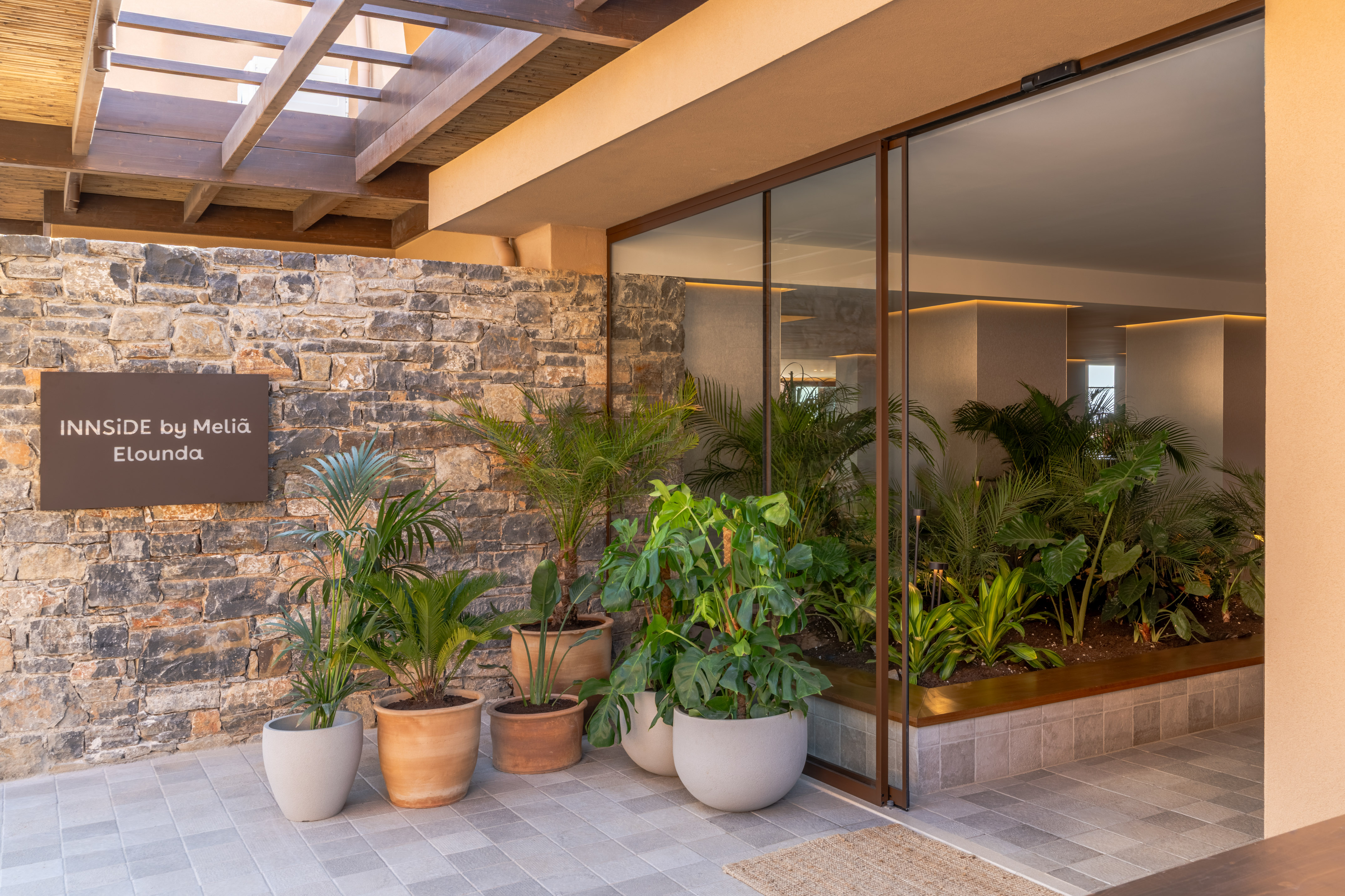 INNSiDE by Meliã Elounda entrance with stone wall and tropical plants.