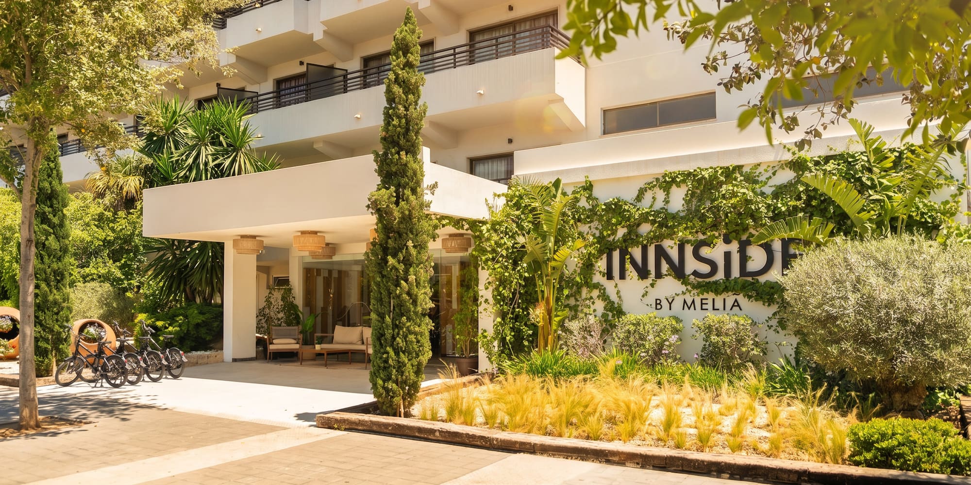 Innside by Meliá hotel entrance, white building, lush green plants, sunny day.