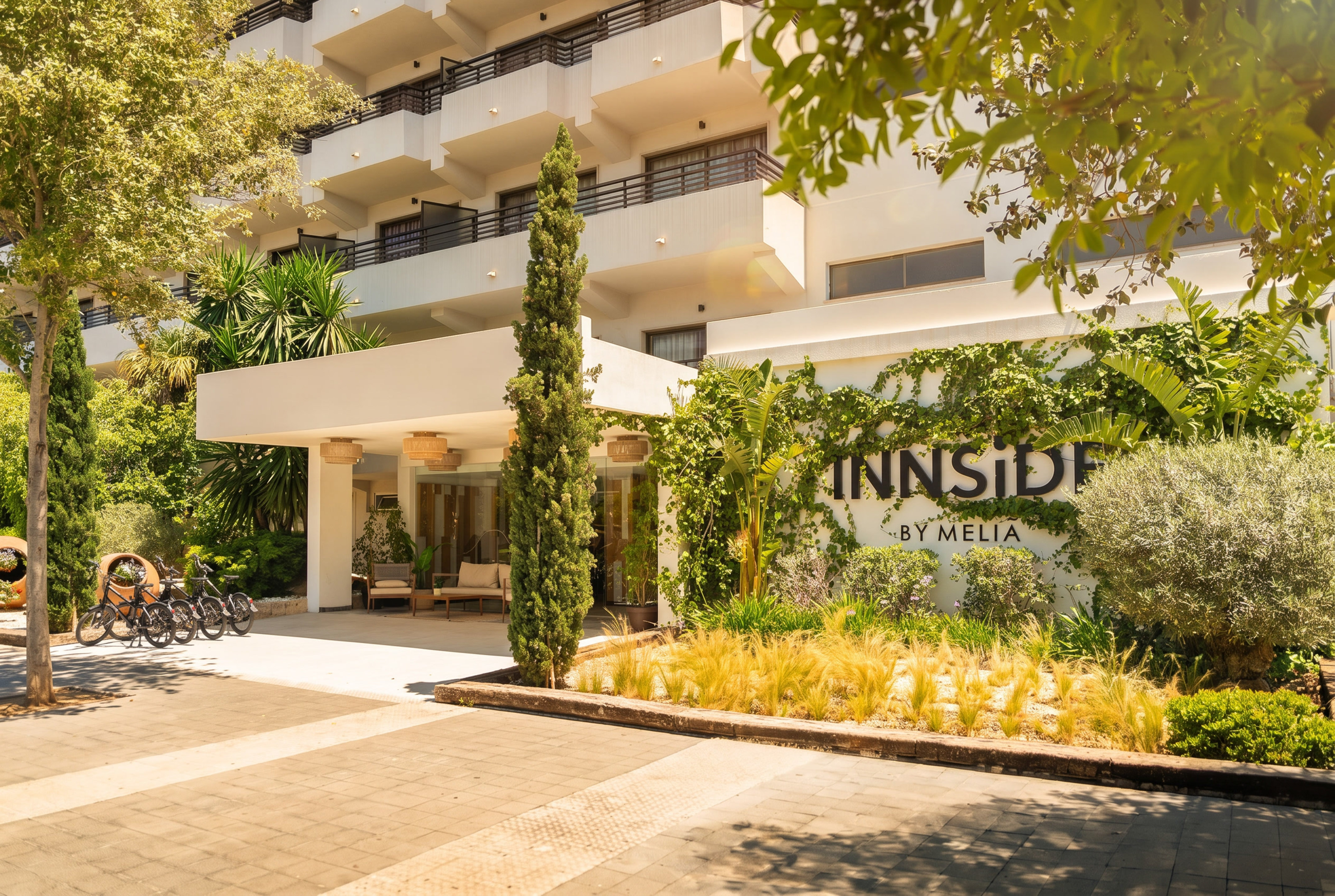 Innside by Meliá hotel entrance, white building, lush green plants, sunny day.