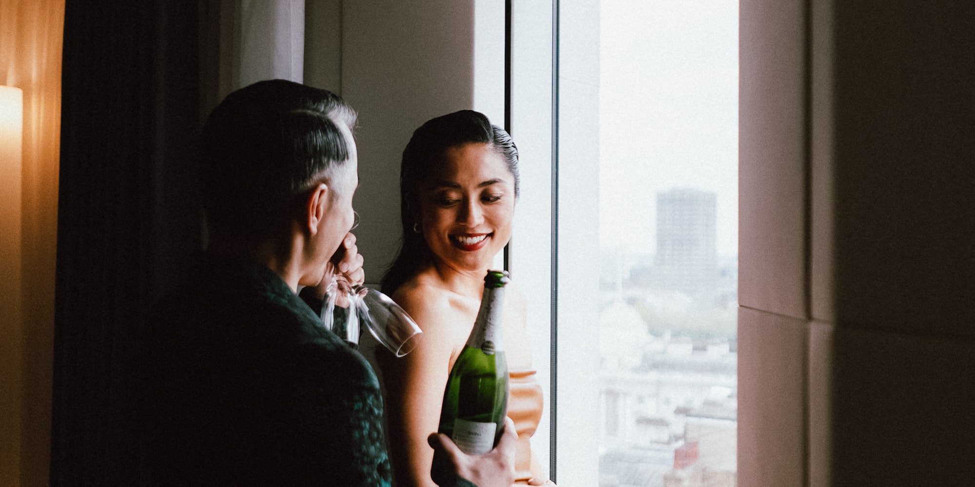 a man holding a bottle of wine and a woman standing in front of a window