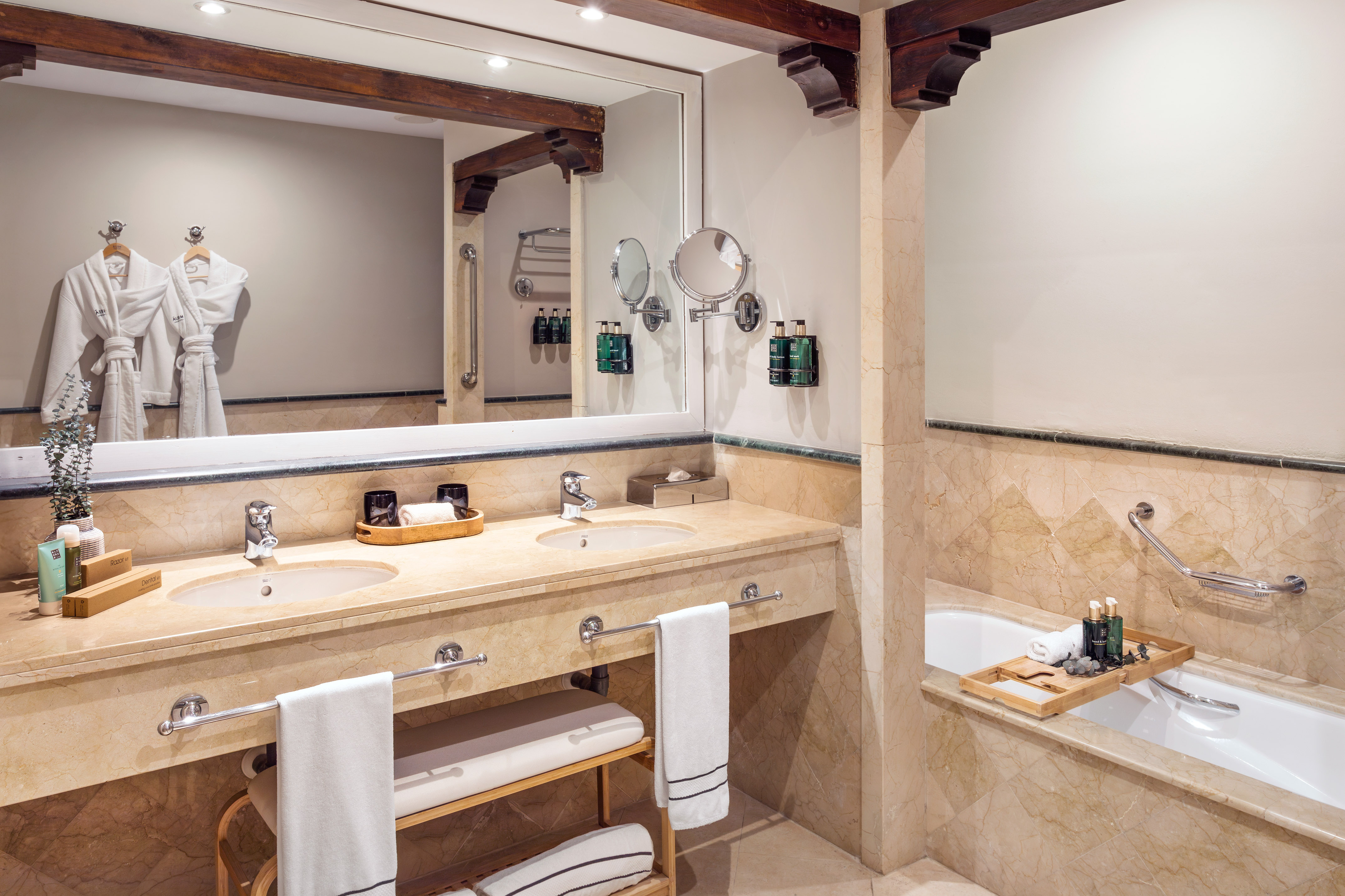 Luxurious marble bathroom with double vanity, two sinks, bathtub, and bathrobes.