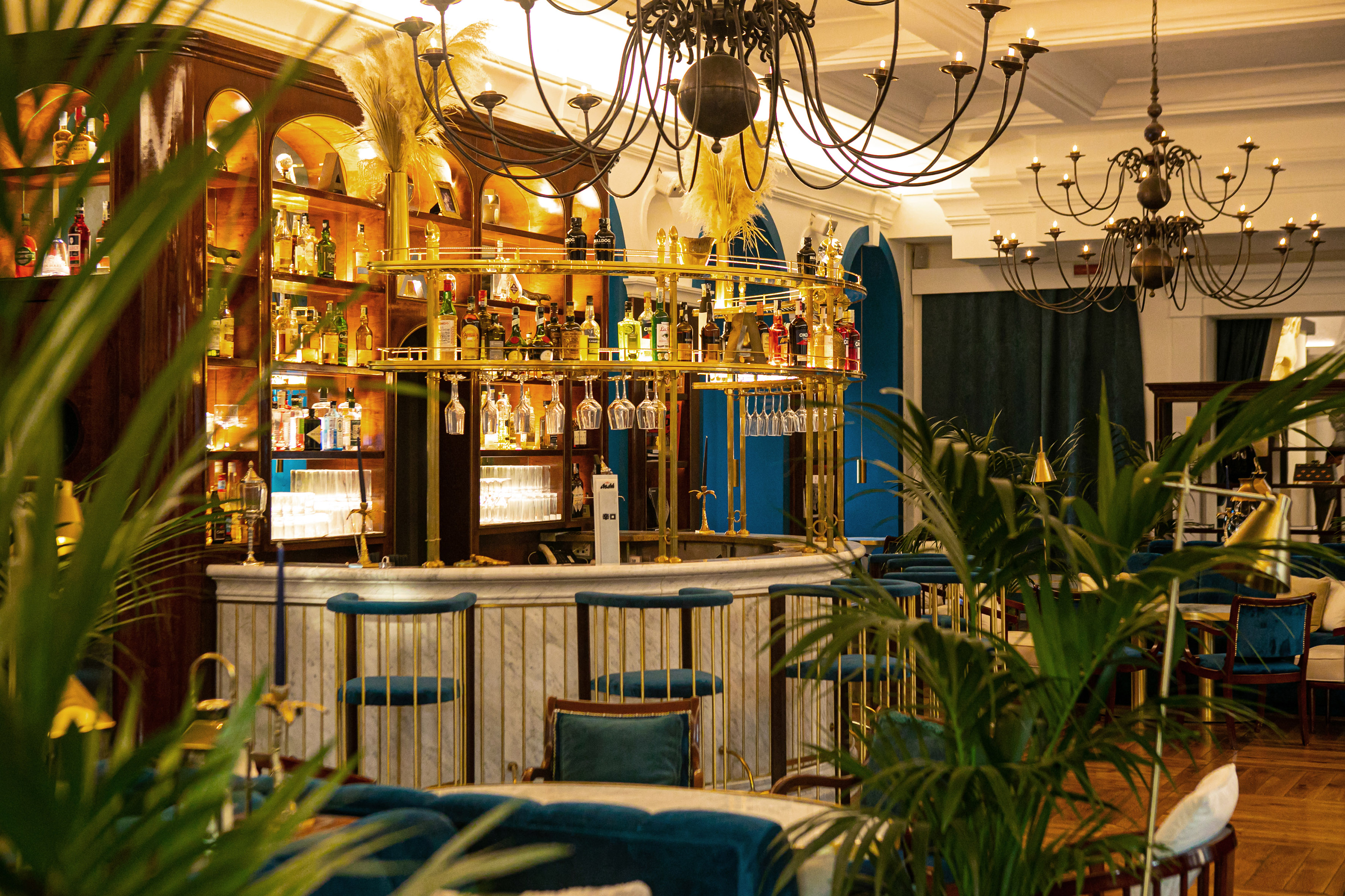 Sophisticated bar with gold accents, marble counter, spirits, and blue seating.