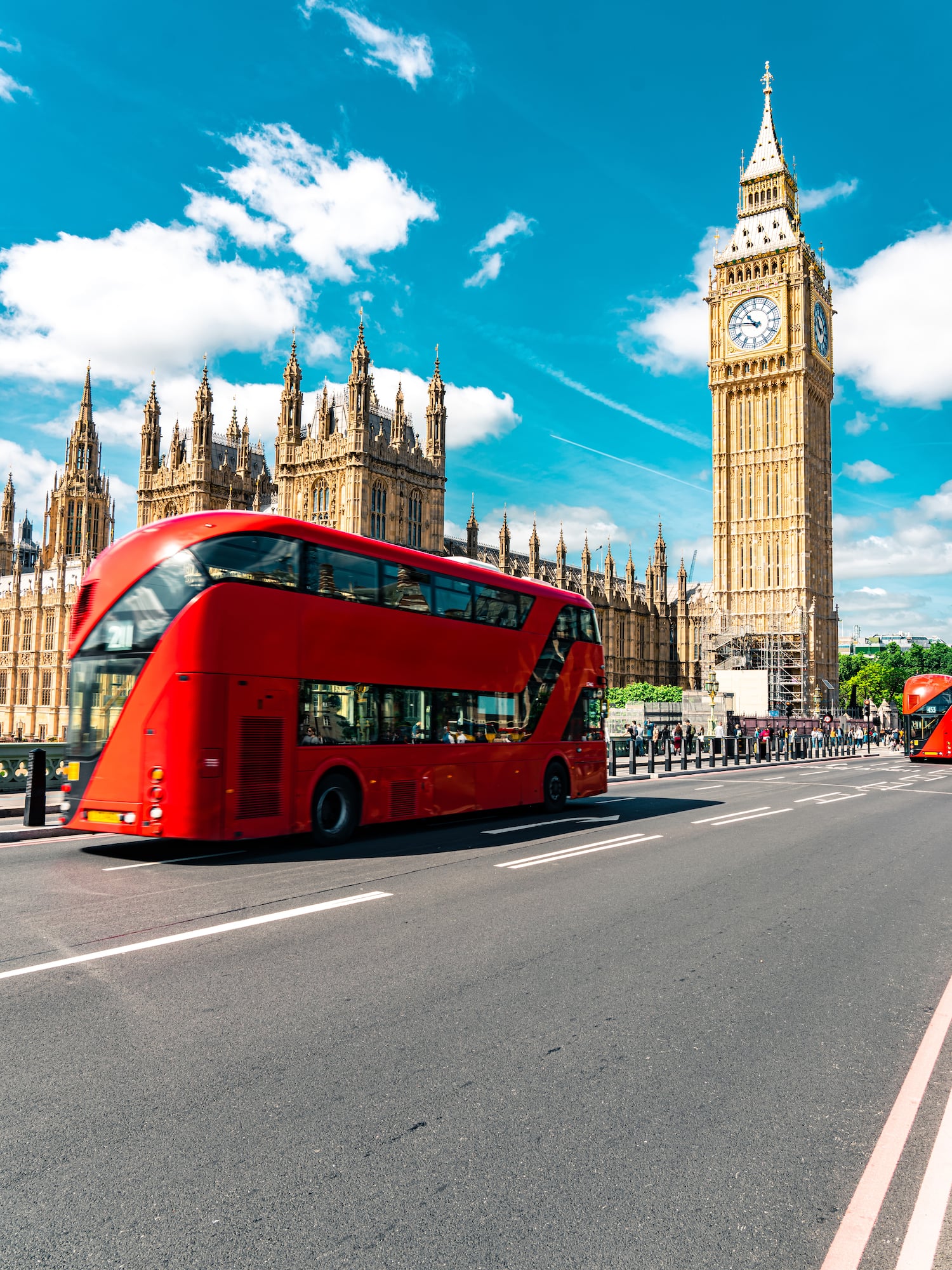 A double-decker bus sits on the road in front of a clock tower.