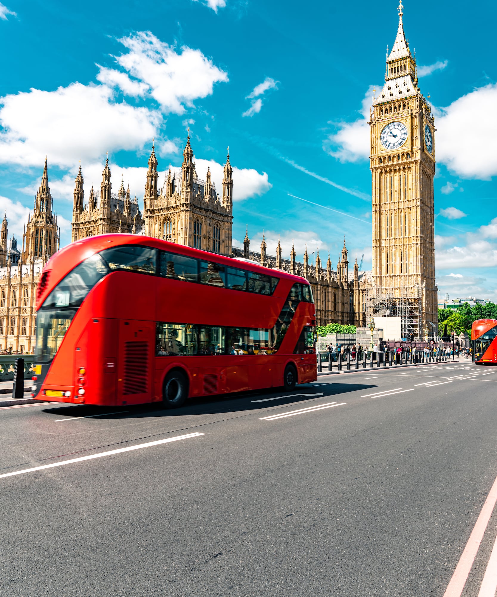 A double-decker bus sits on the road in front of a clock tower.