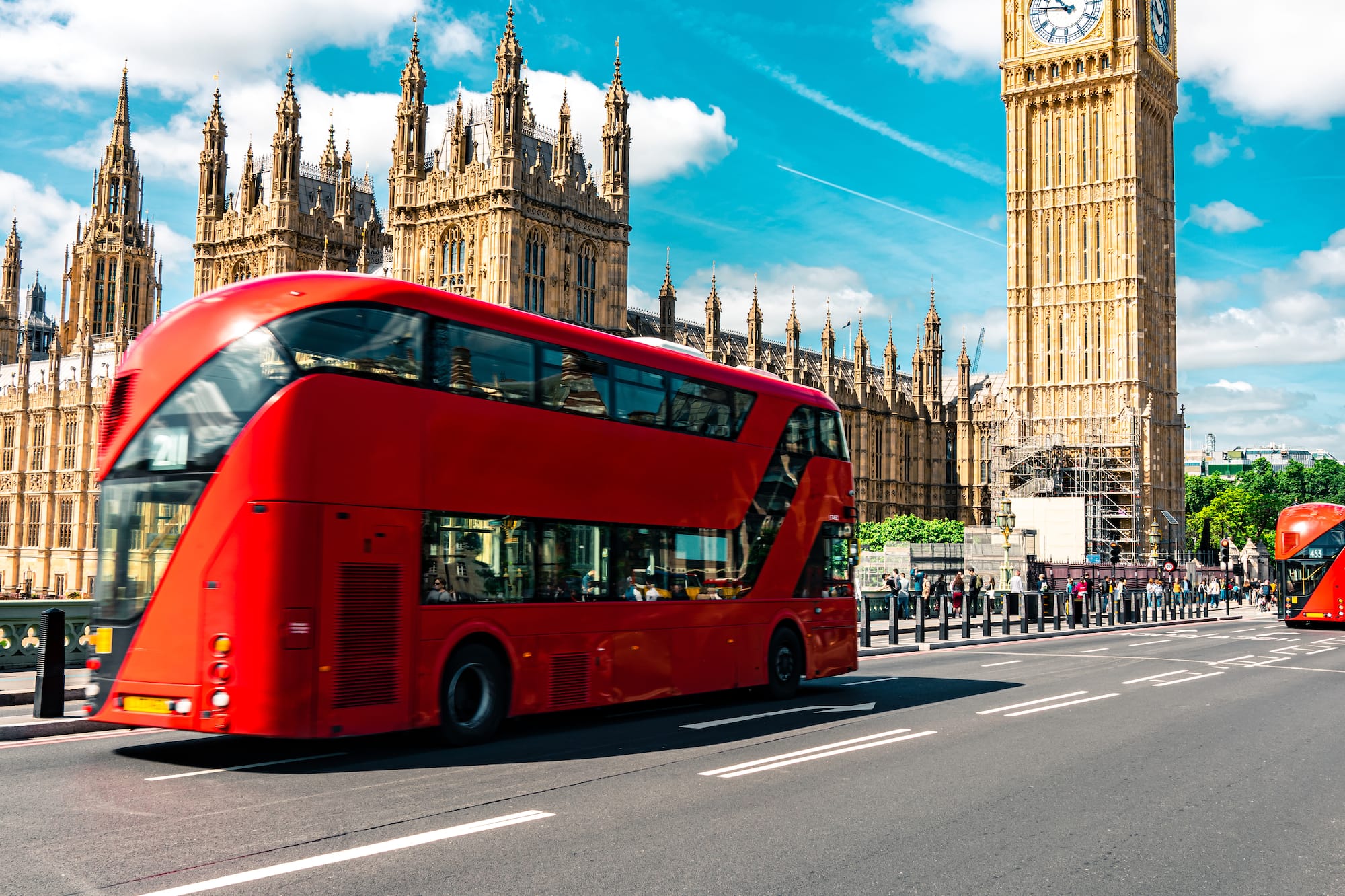 A double-decker bus on a street in front of a clock tower.