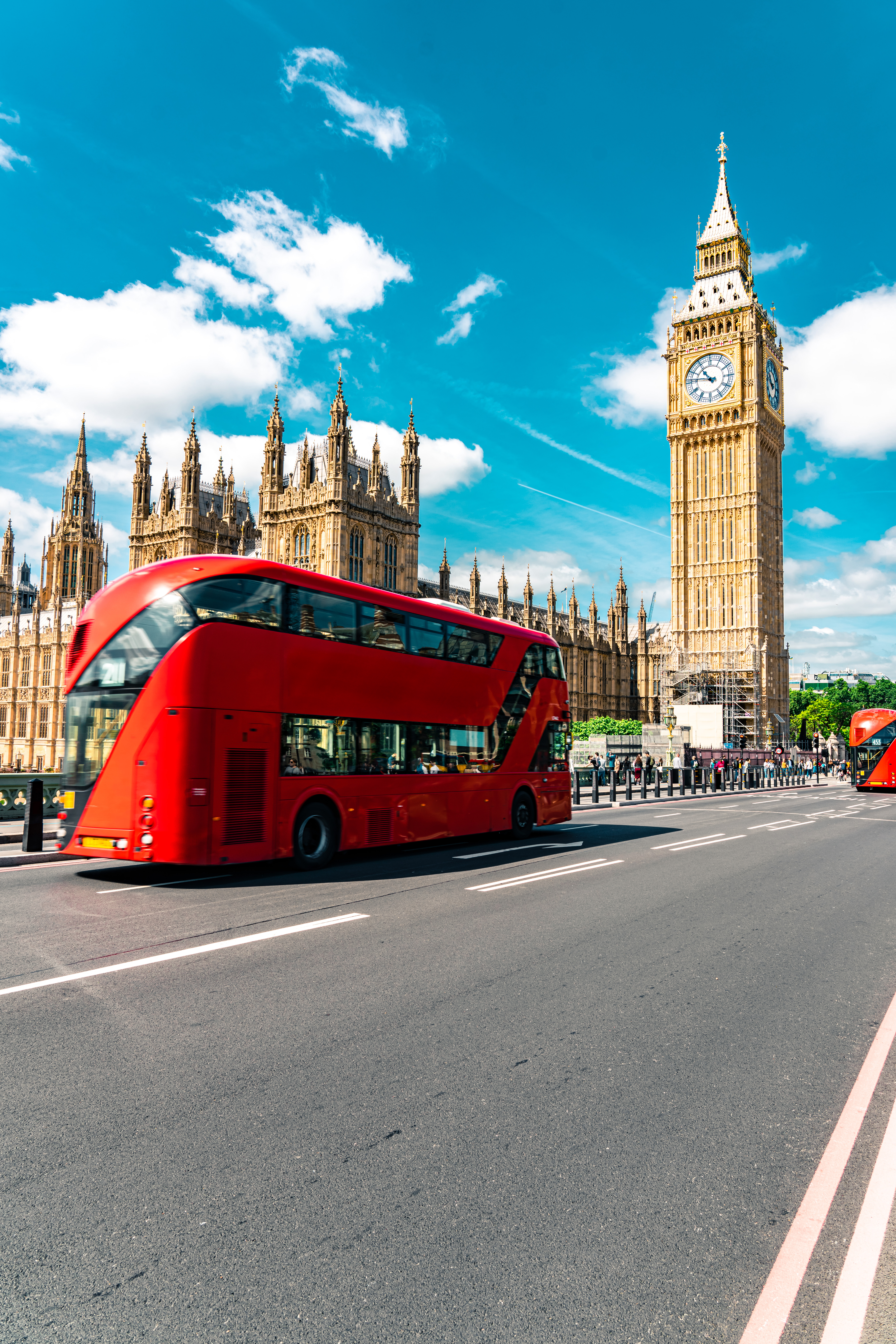 A double-decker bus sits on the road in front of a clock tower.