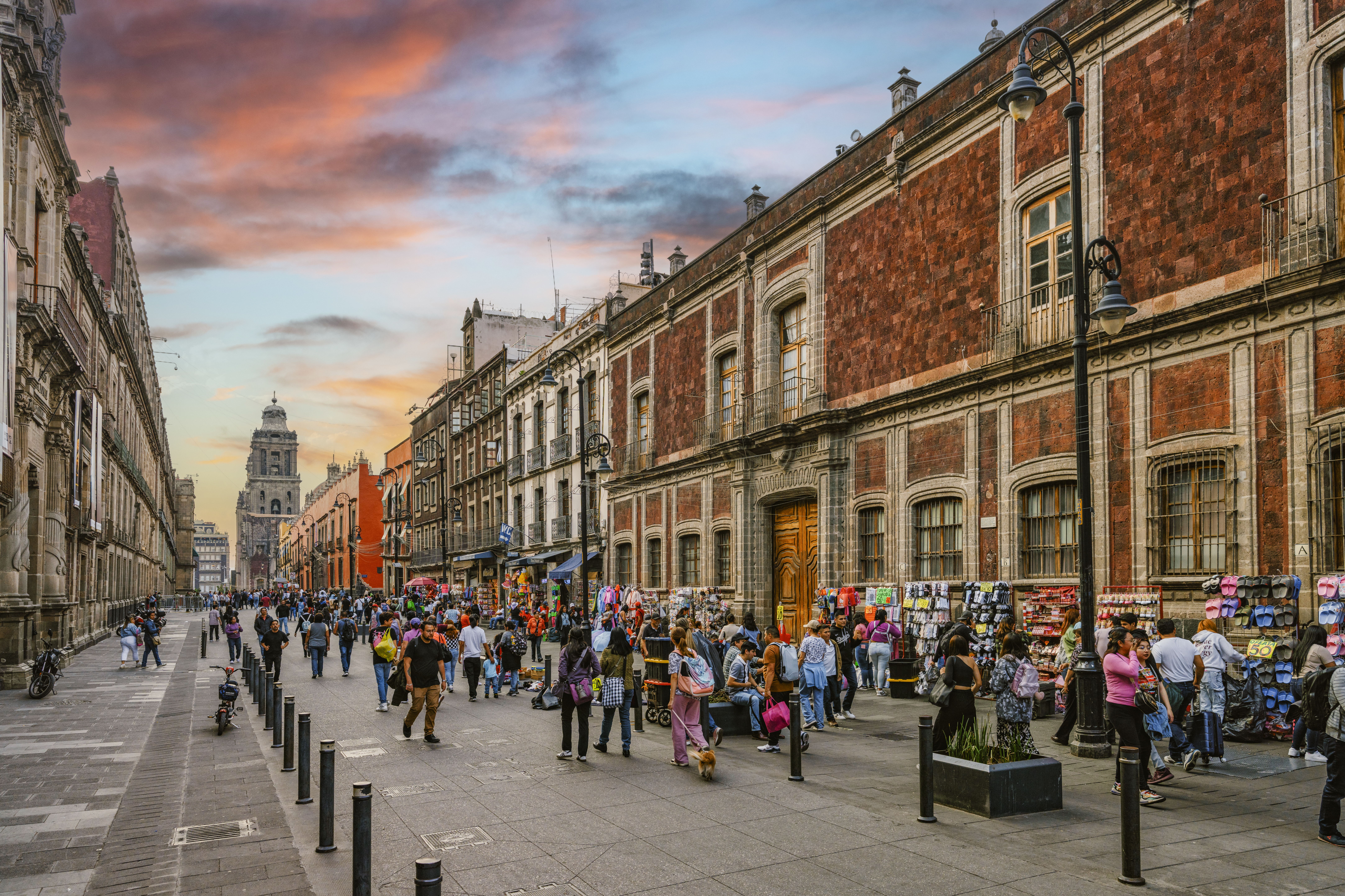 Calle concurrida en CDMX, edificios históricos, Catedral, cielo atardecer.
