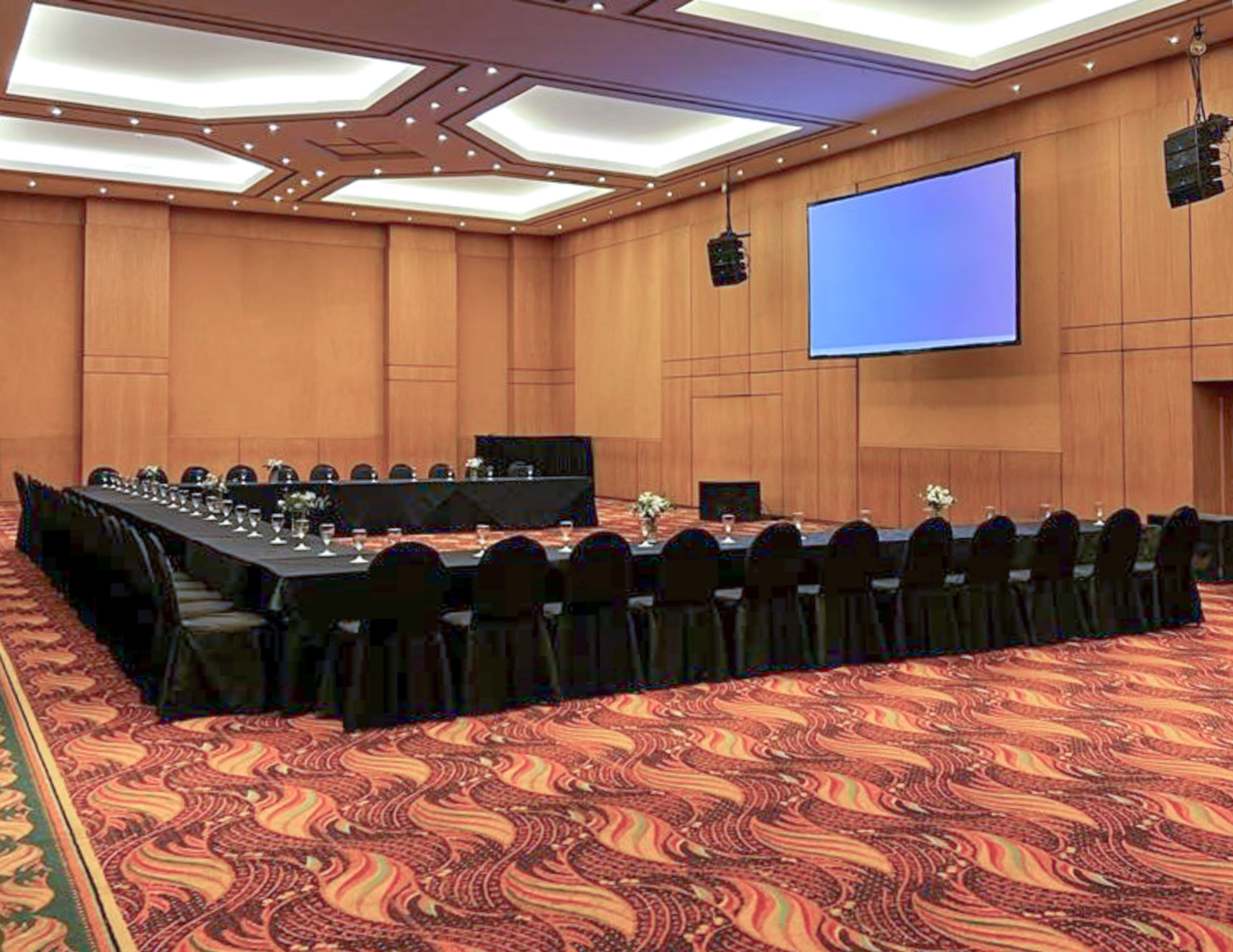 U-shaped meeting room setup with large screen, speakers, and patterned carpet.