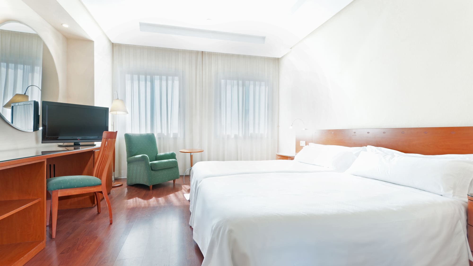 Clean hotel room with twin beds, wooden desk, TV, and green armchair.