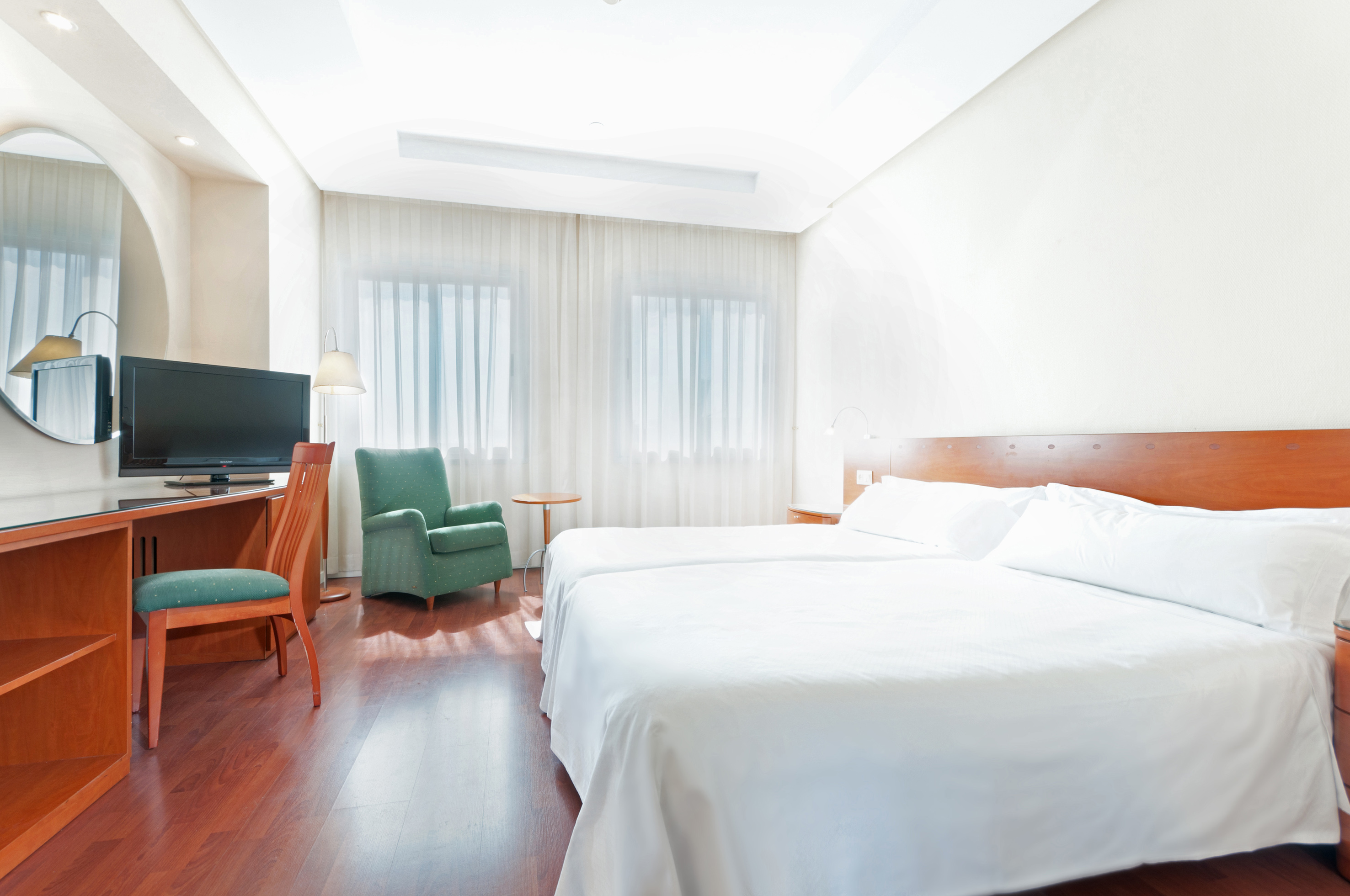 Clean hotel room with twin beds, wooden desk, TV, and green armchair.