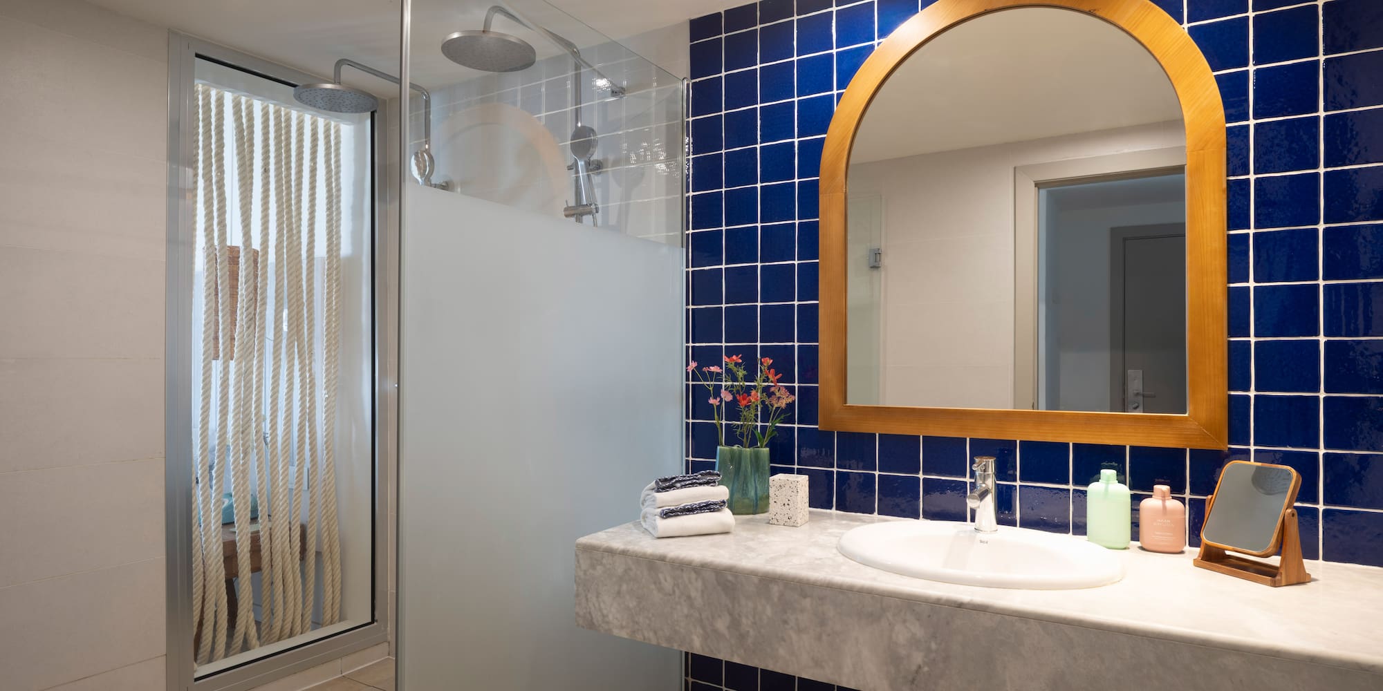 Baño moderno con ducha, azulejos azules, espejo de madera y lavabo de mármol.