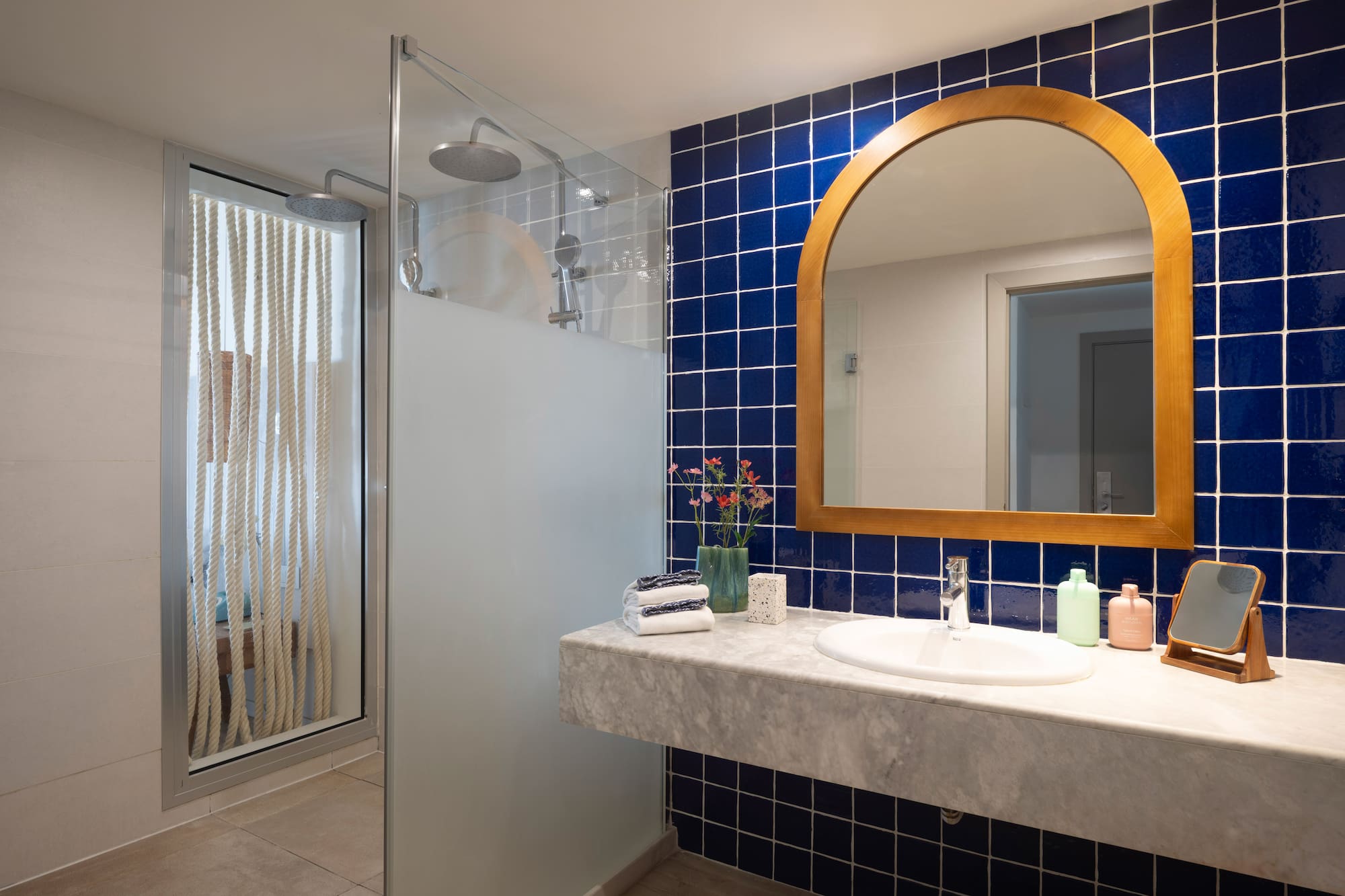 Baño moderno con ducha, azulejos azules, espejo de madera y lavabo de mármol.