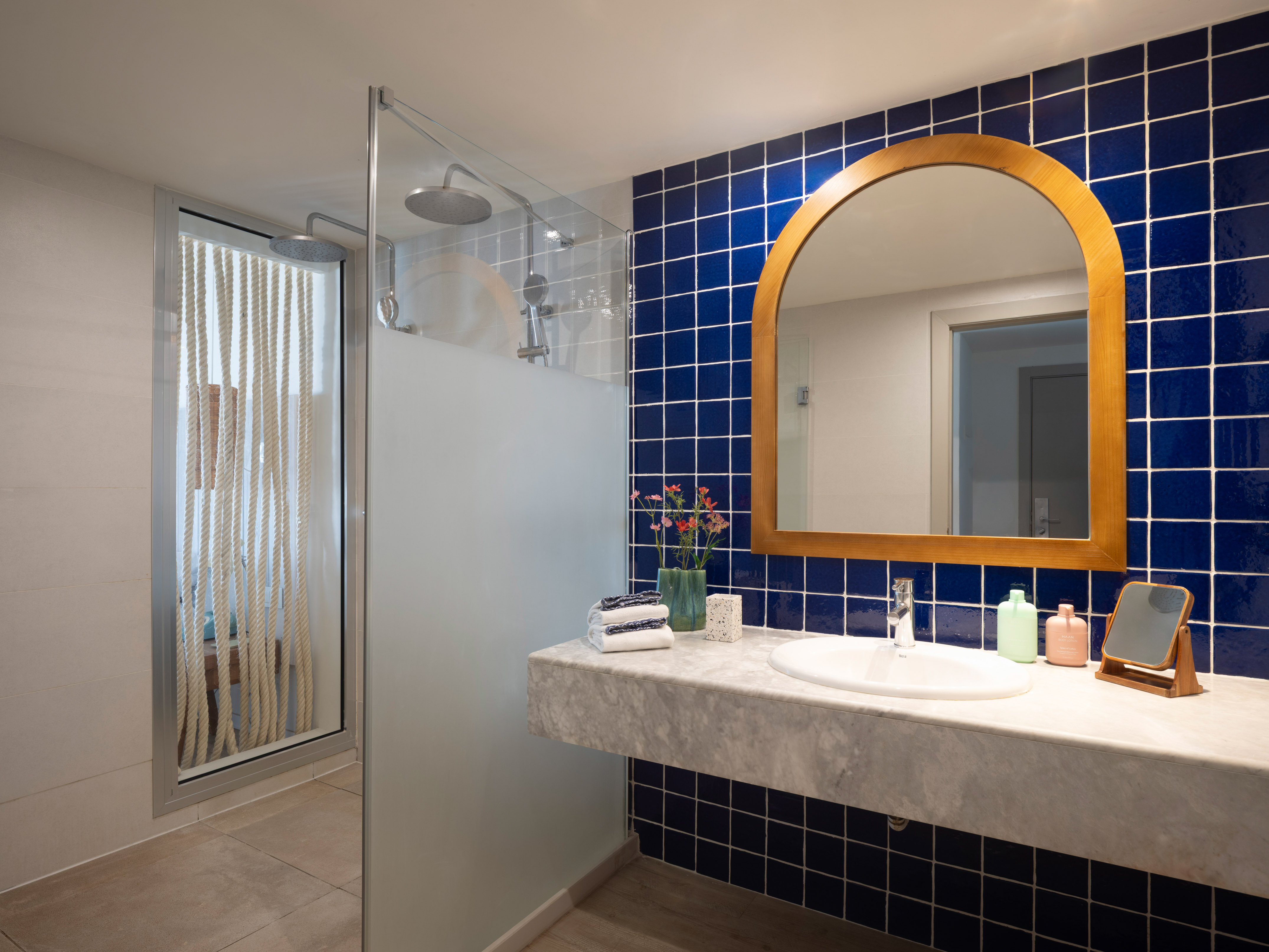 Baño moderno con ducha, azulejos azules, espejo de madera y lavabo de mármol.