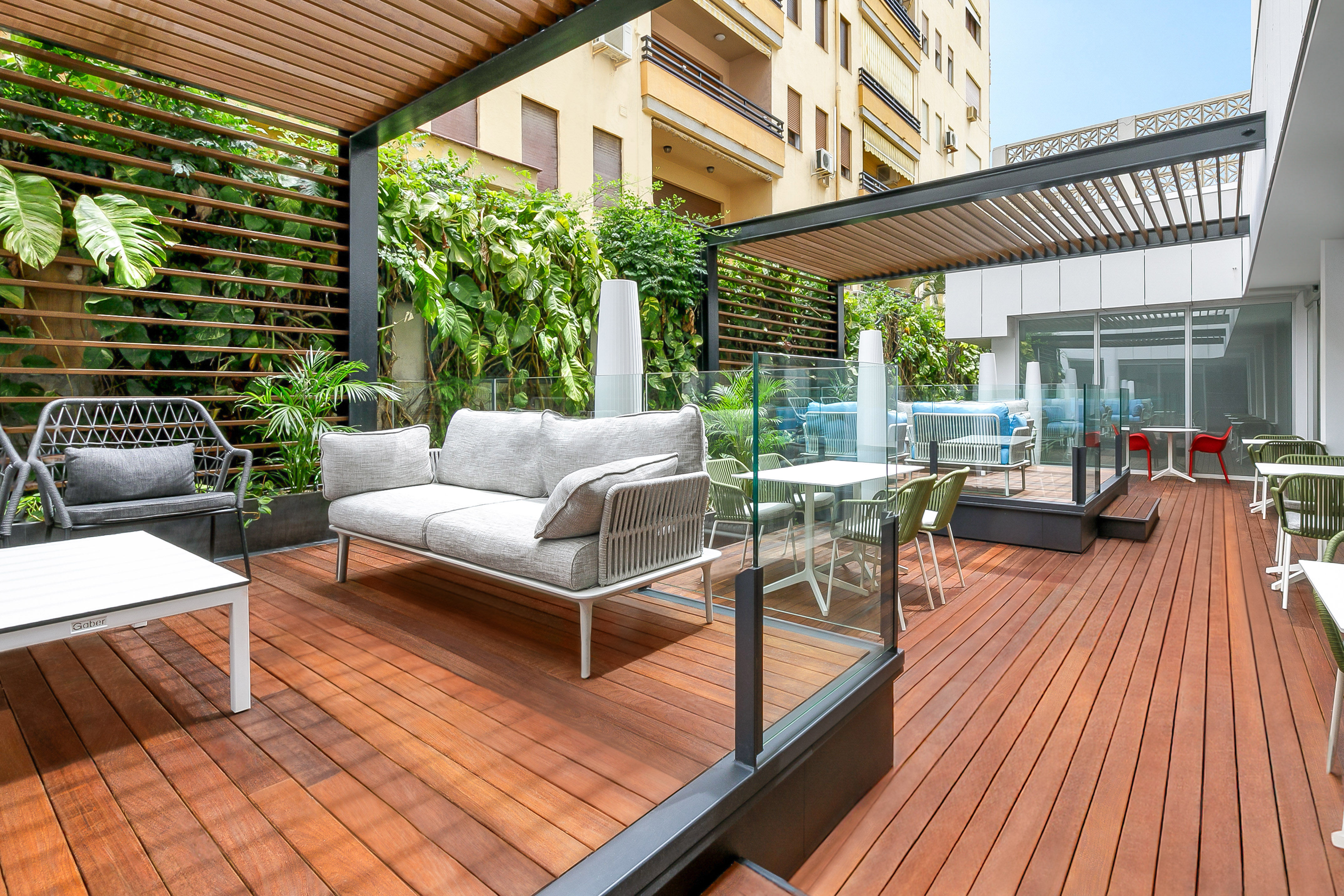 Modern outdoor patio deck with lounge seating, pergola, and lush greenery.