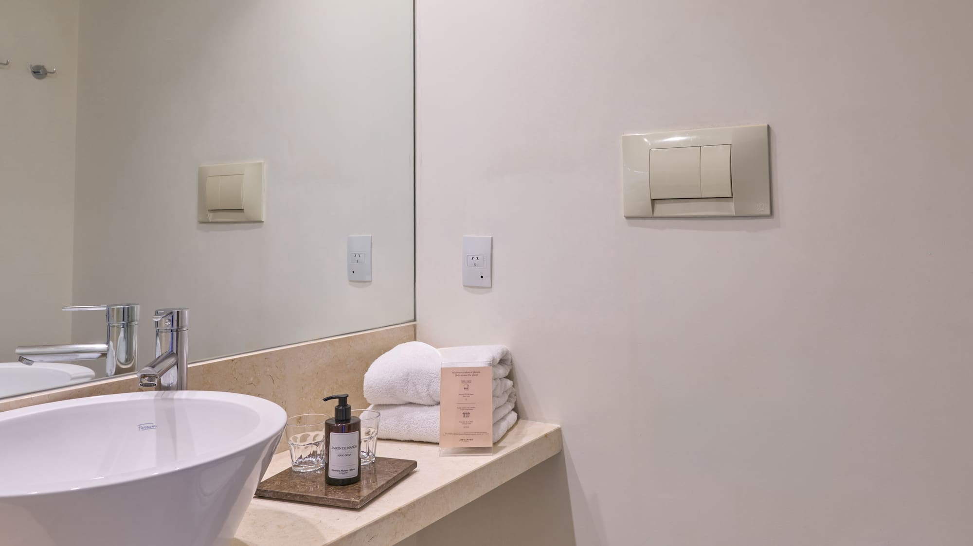 Bright modern hotel bathroom with white vessel sink, vanity, mirror, and toilet.