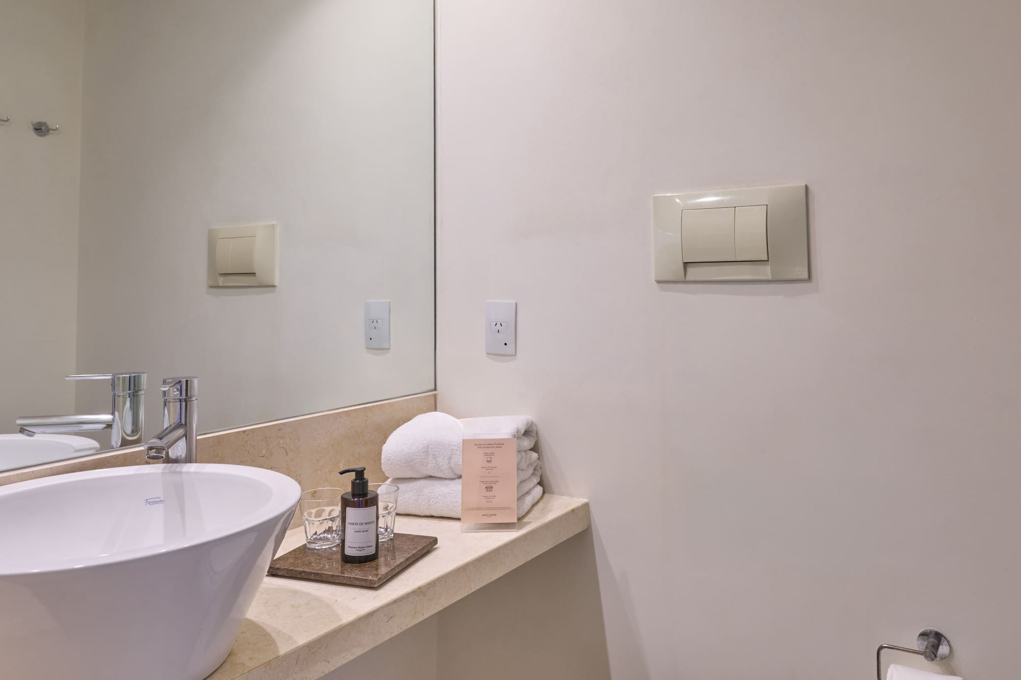 Bright modern hotel bathroom with white vessel sink, vanity, mirror, and toilet.