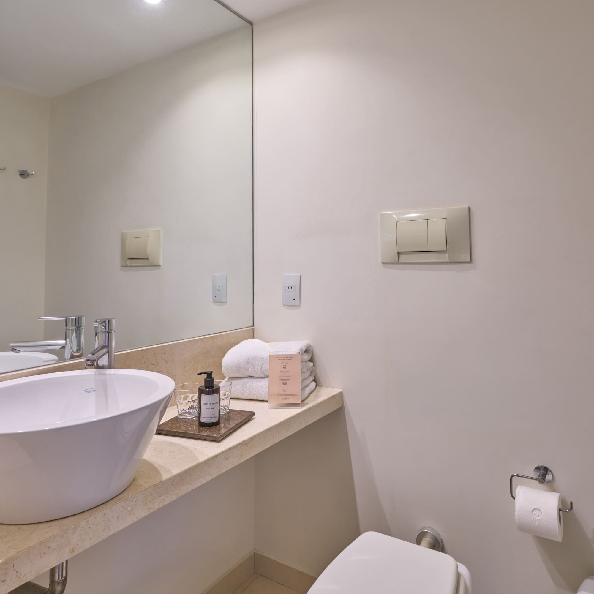 Bright modern hotel bathroom with white vessel sink, vanity, mirror, and toilet.
