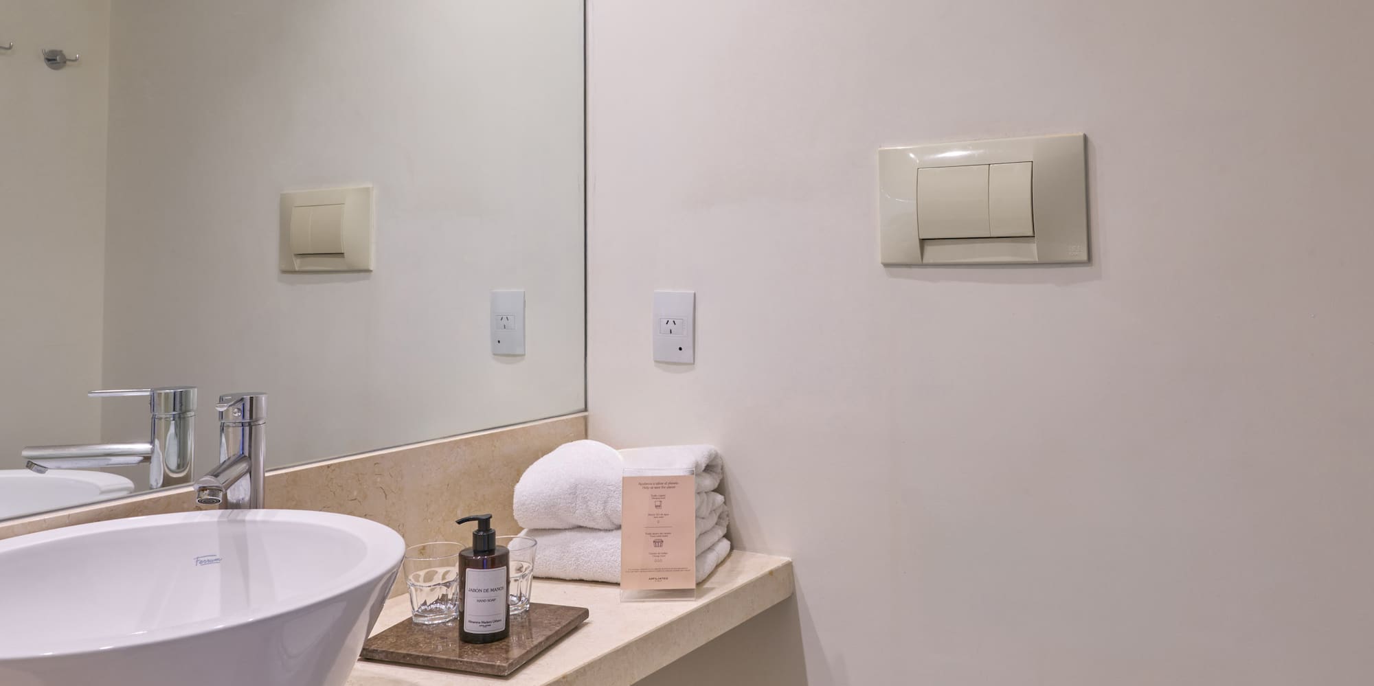 Bright modern hotel bathroom with white vessel sink, vanity, mirror, and toilet.