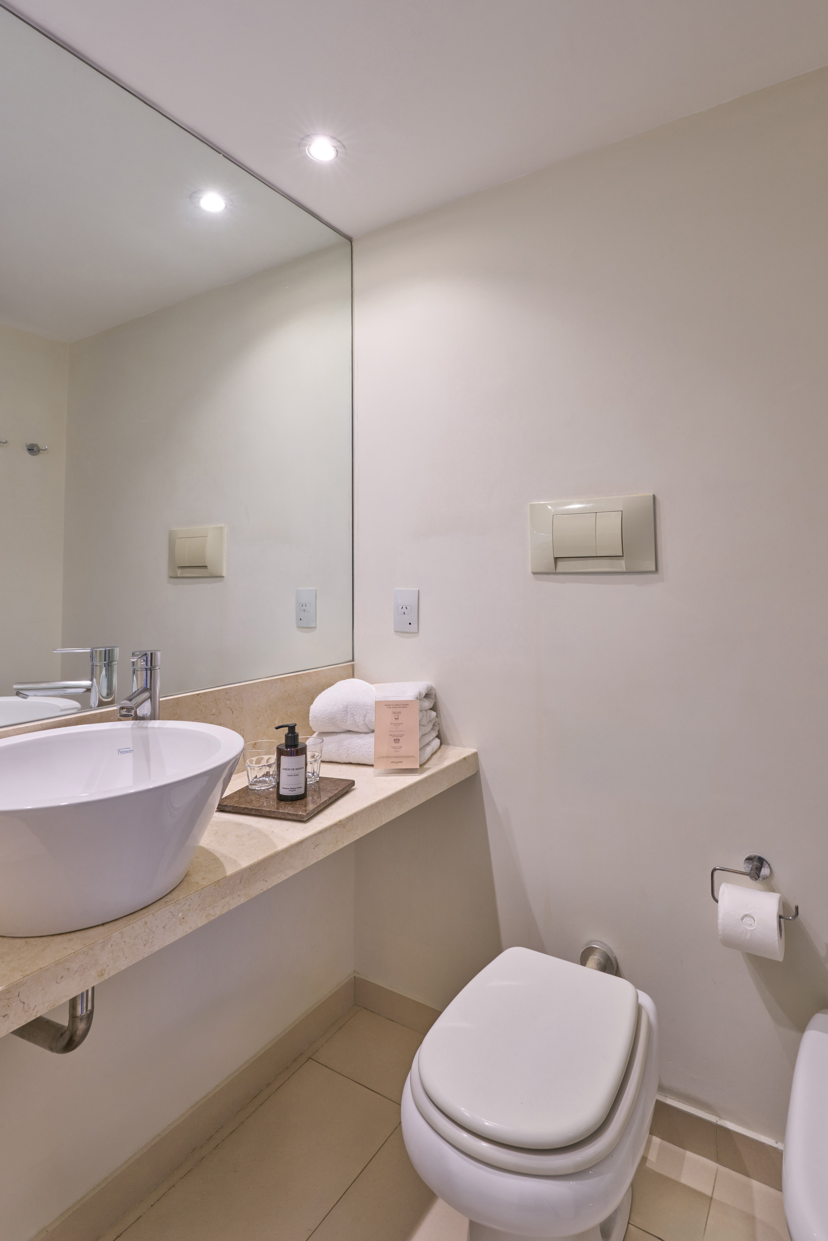 Bright modern hotel bathroom with white vessel sink, vanity, mirror, and toilet.