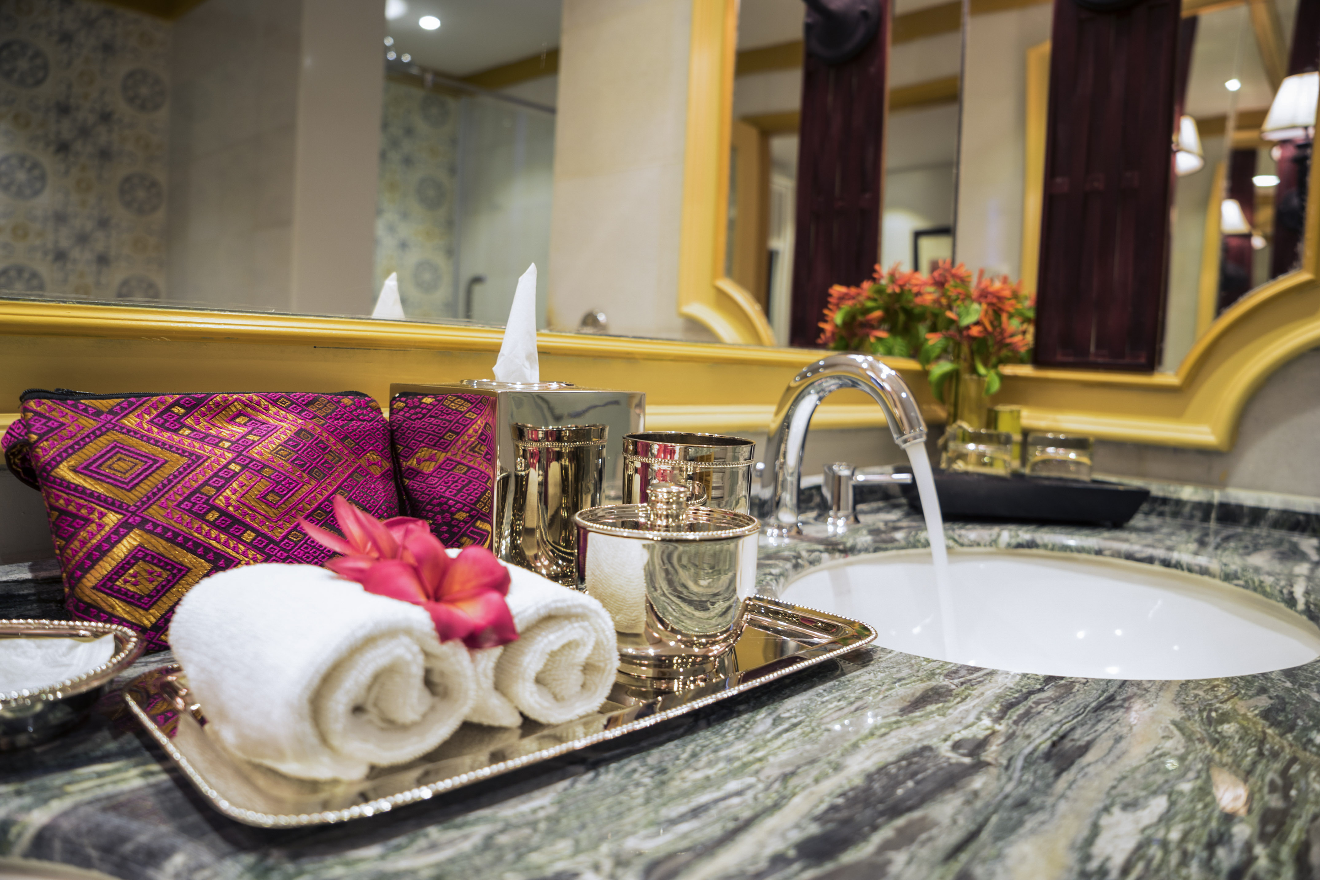 Marble bathroom vanity with chrome faucet, rolled towels, and decorative pouch.
