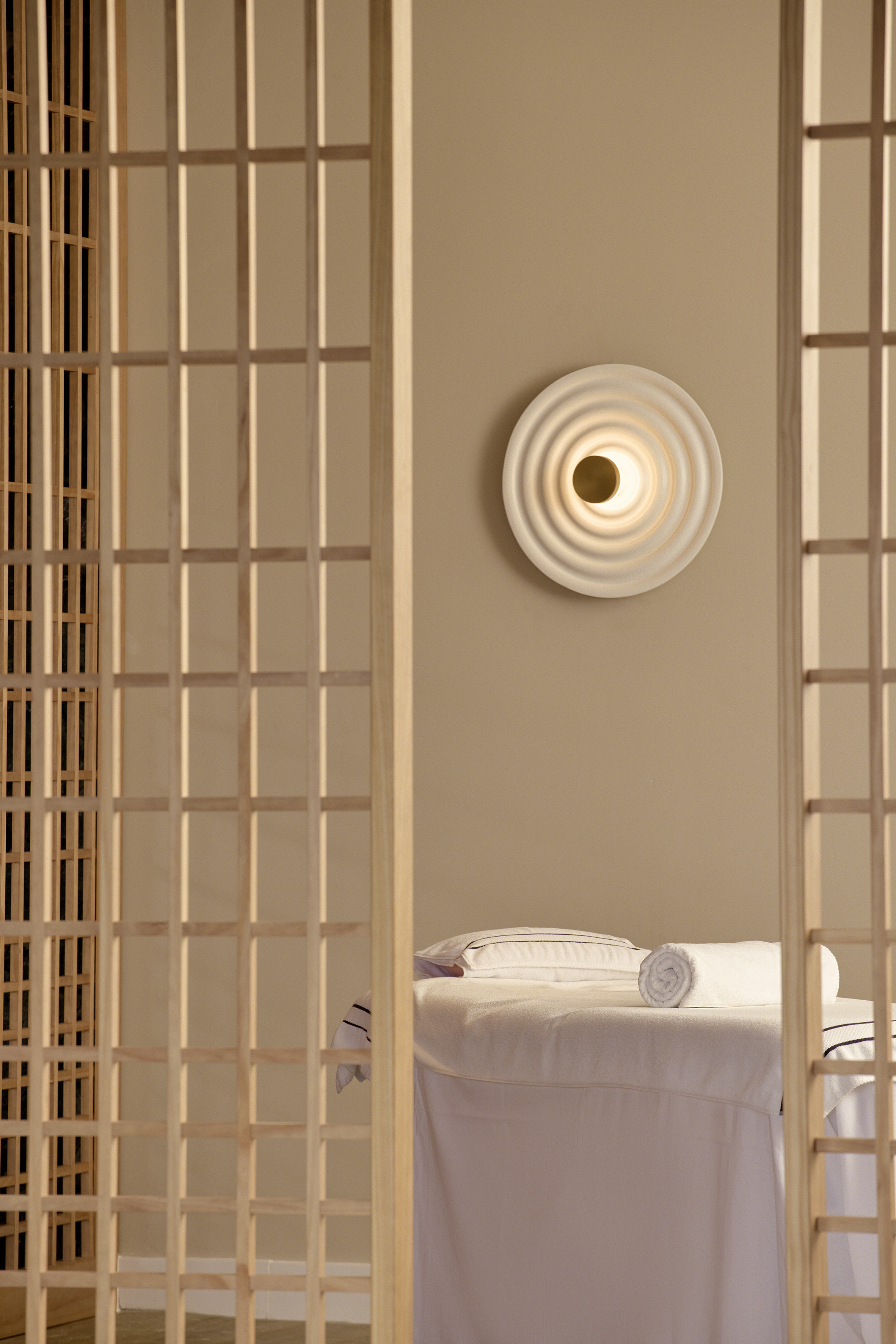 Spa room with massage table, wooden screens, and modern wall light.