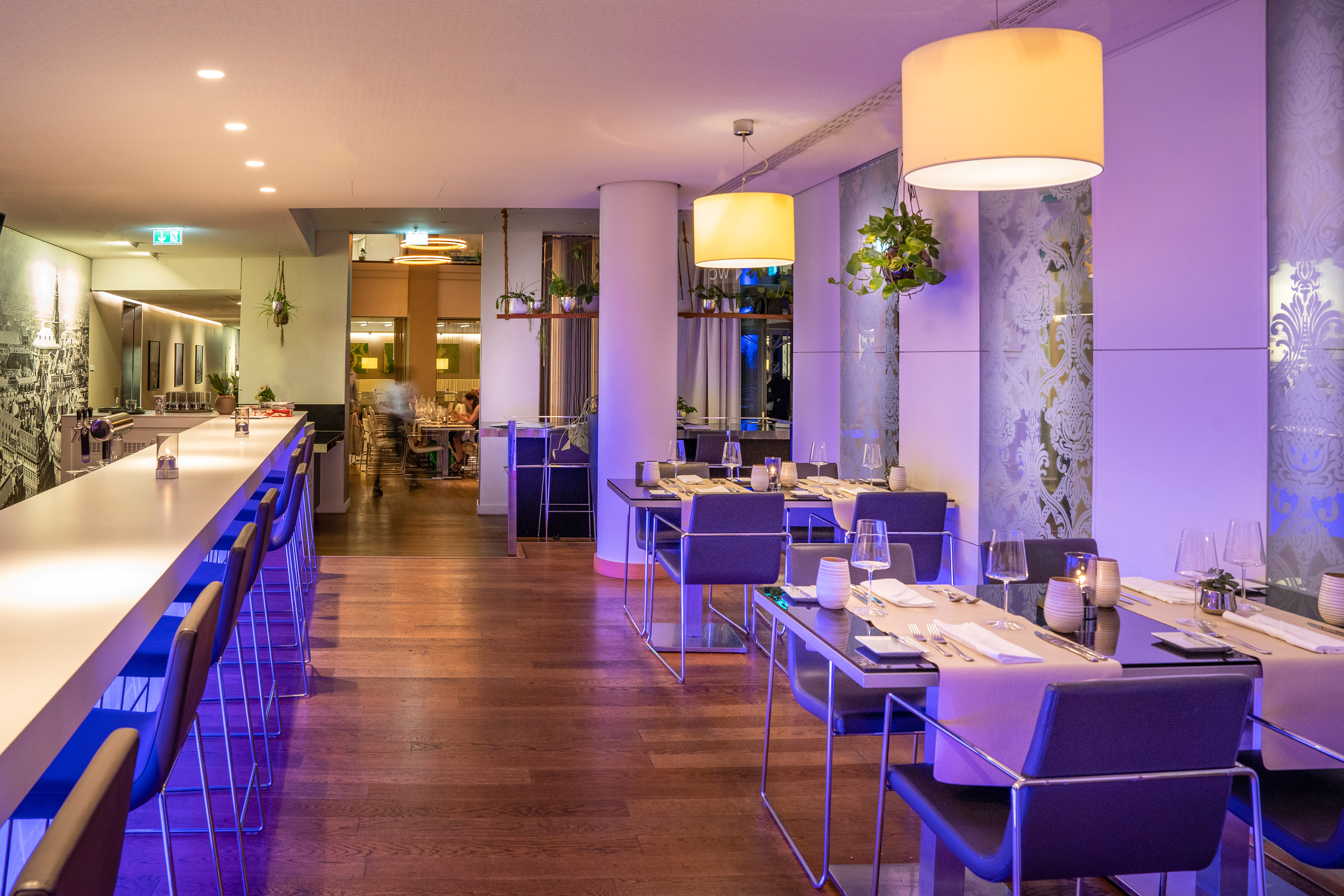 Elegant restaurant bar with modern dining tables, purple ambient lighting.