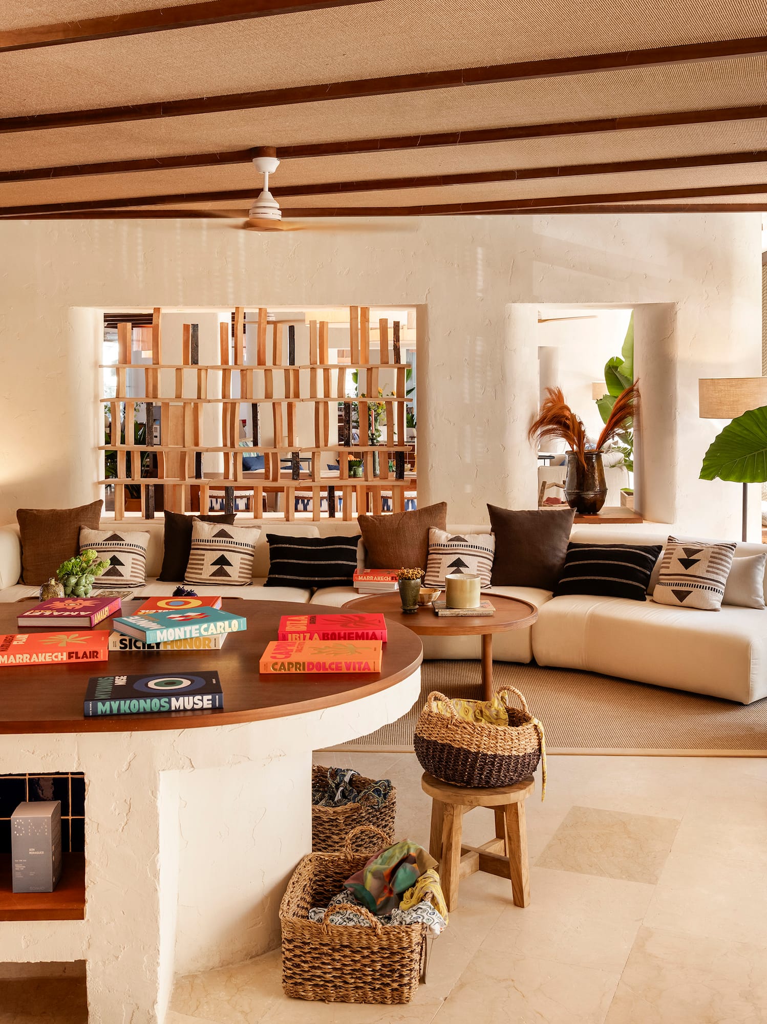 Elegant resort lounge with white sofa, coffee table books, lush plant, wood ceiling.